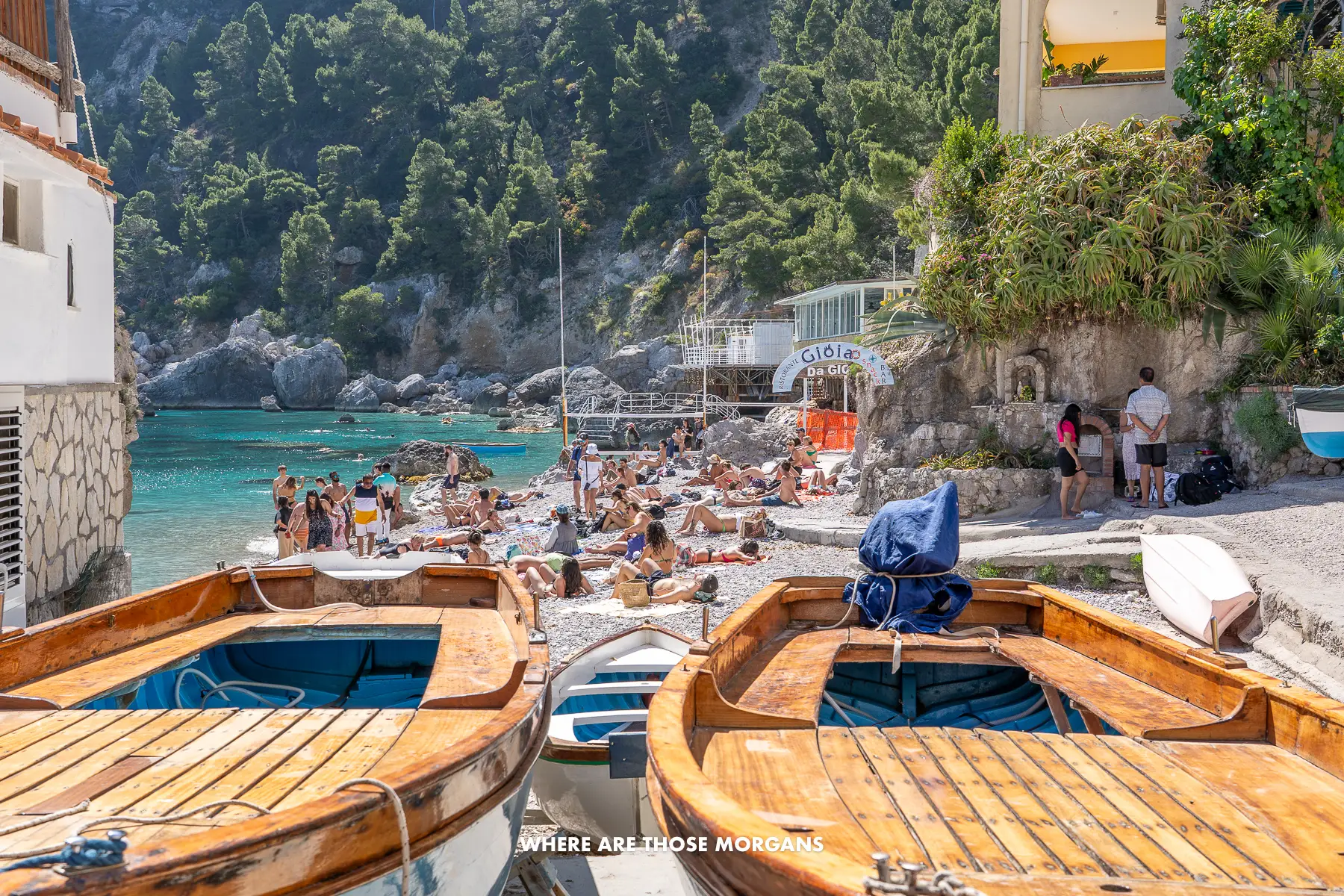 Photo of two small wooden boats on a pebble beach with sunbathers behind