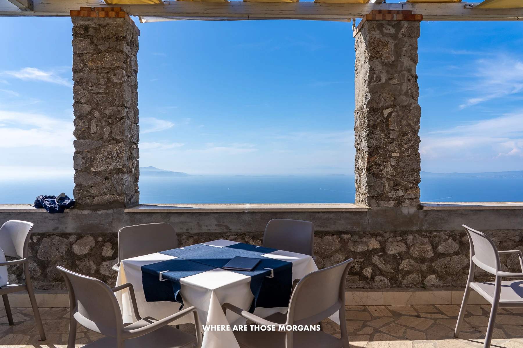 Photo of a restaurant at the top of Monte Solaro in Capri with tables, chairs and stone structure revealing huge gaps for windows overlooking the sea