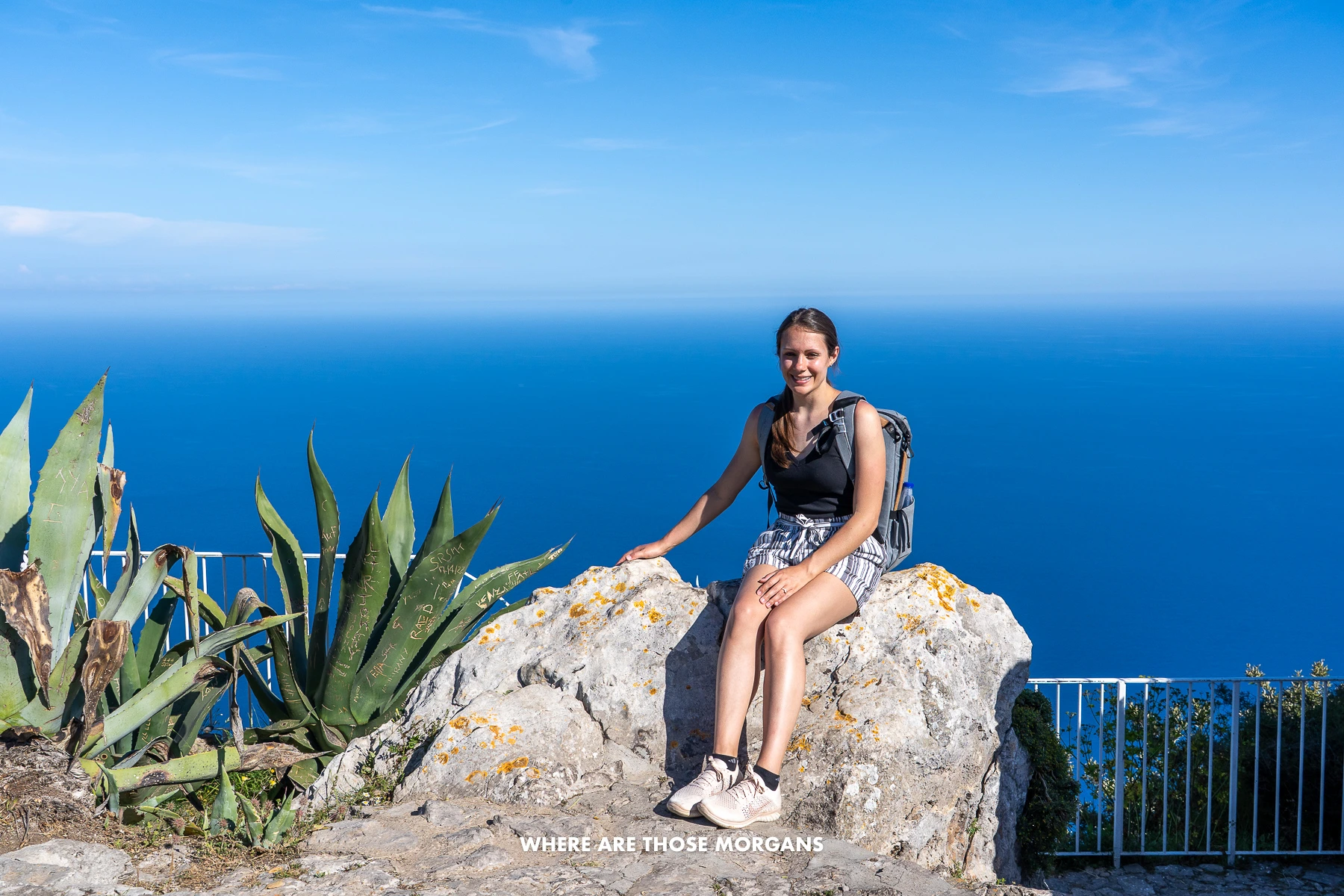 Photo of Kristen from Where Are Those Morgans at the top of Monte Solaro sat on a rock next to a plant with immense views over the sea and sky behind