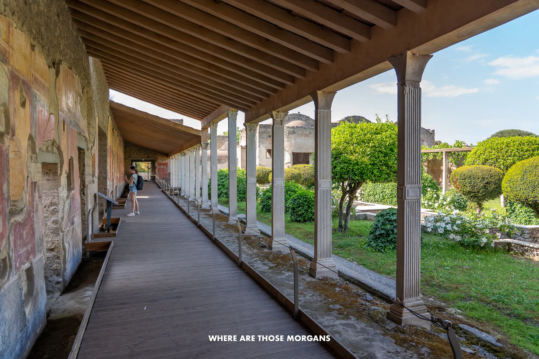 Photo of a covered walkway next to a garden inside a ruin in Italy