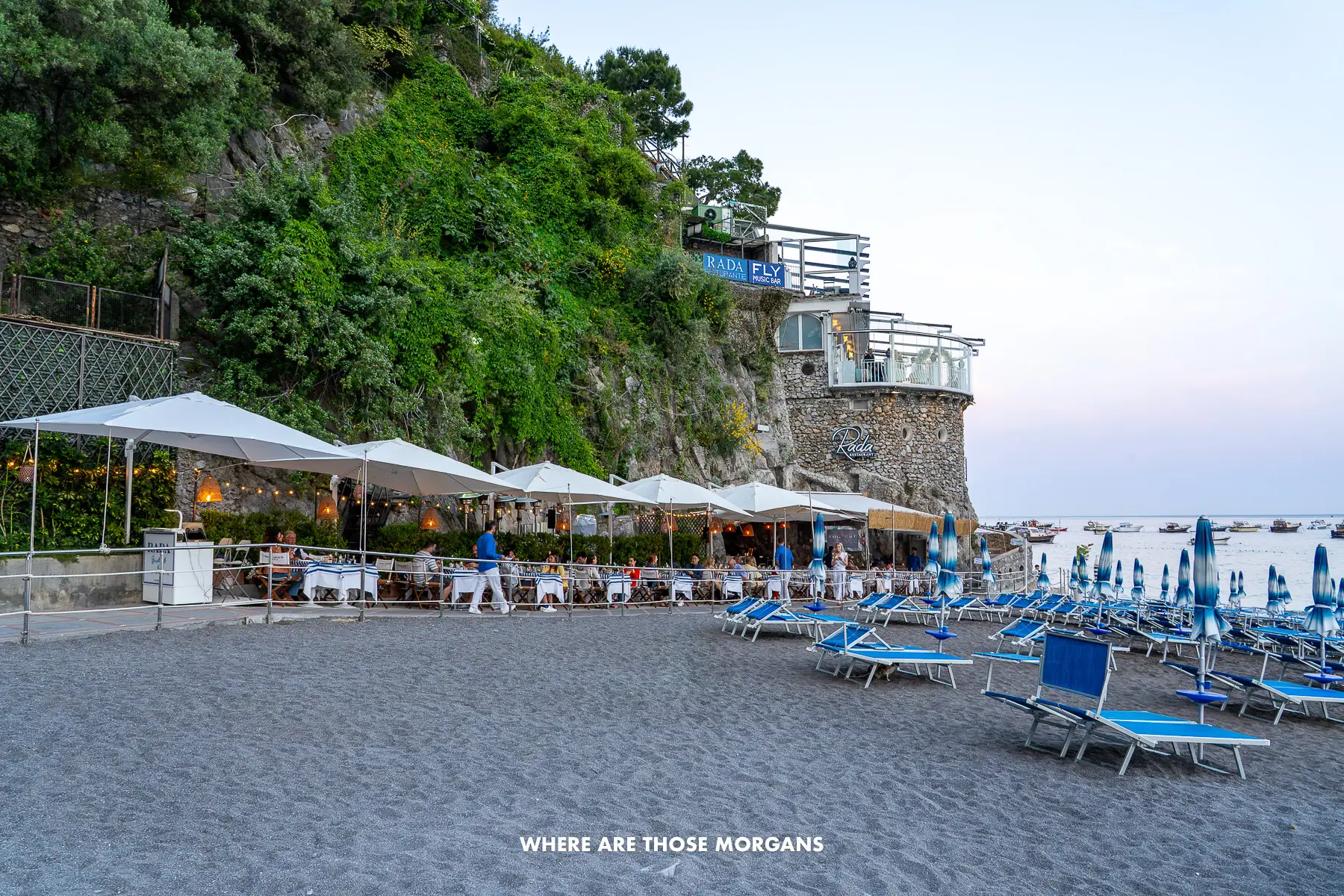 Photo of a beach and sun loungers next to a restaurant and small stone fort on the seafront
