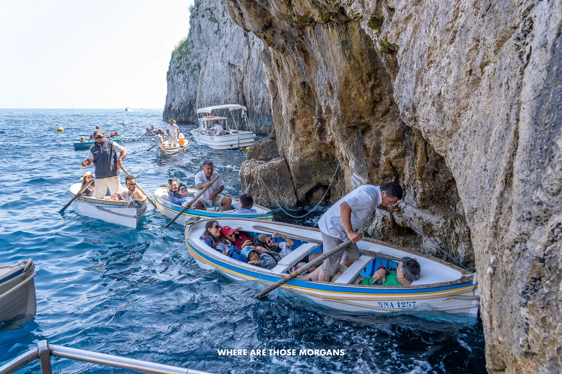 Photo of several boats lining up to go inside a sea cave with tourists being taken in by oarsmen