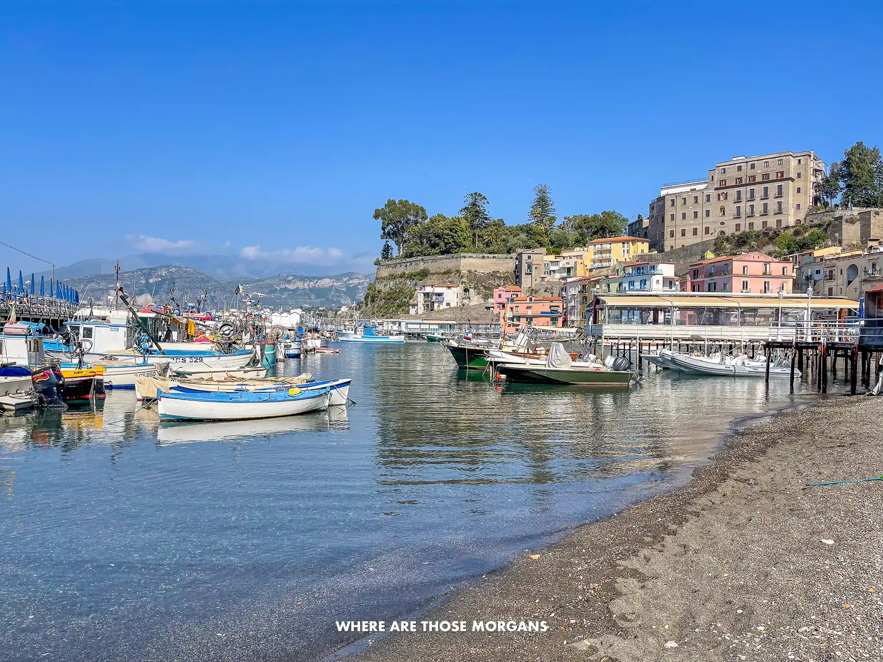 Photo of a pebble beach with small boats floating in a bay in the Gulf of Naples