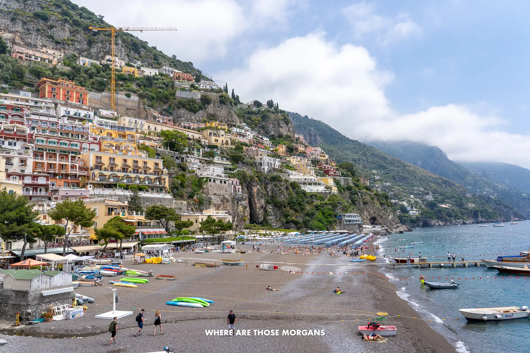 Photo of Marina Grande Beach in Positano with tourists walking on the pebbles next to the sea and buildings from the town perched on the cliffside