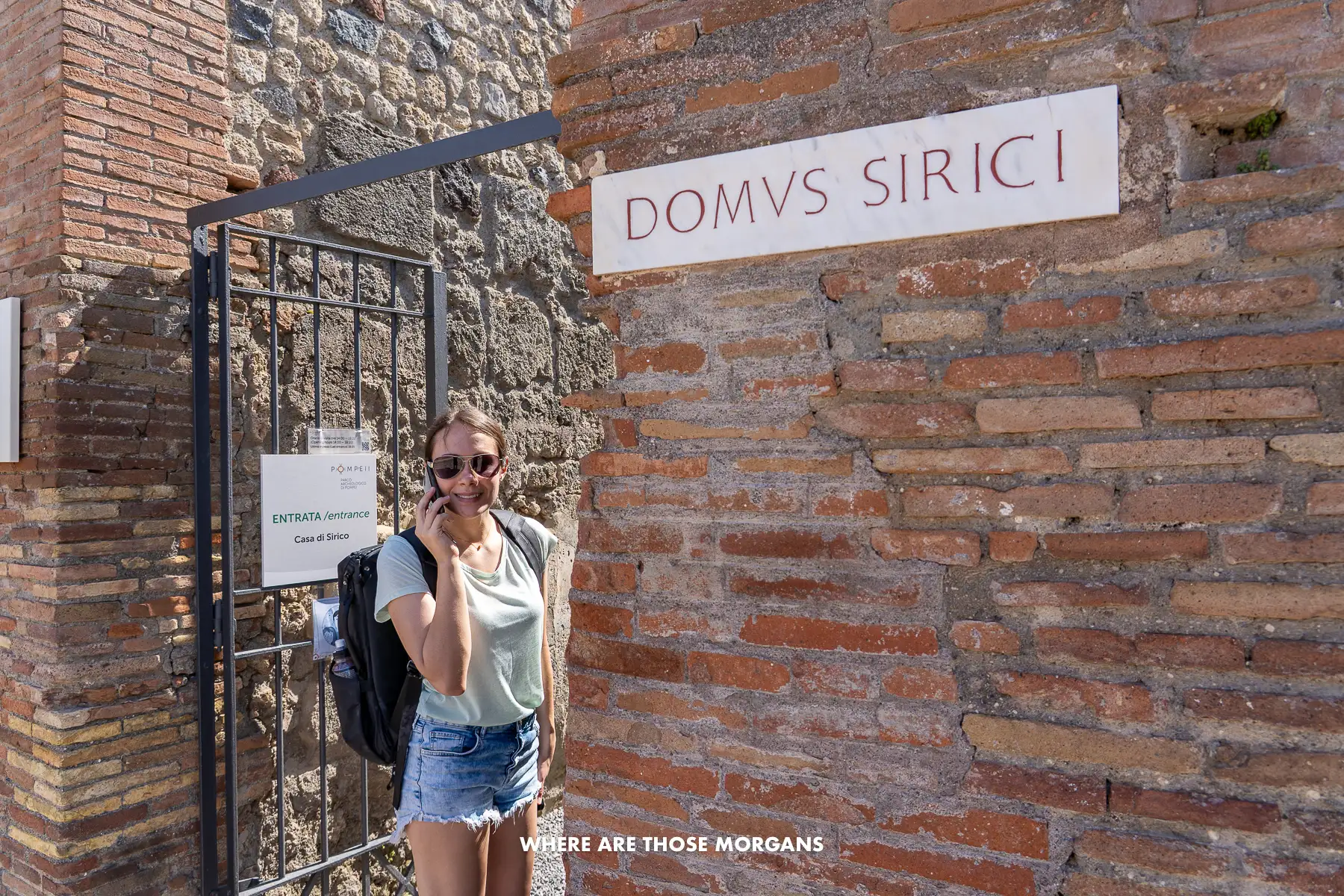 Photo of Kristen from Where Are Those Morgans listening to an audio guide at a gate between brick walls in Pompeii