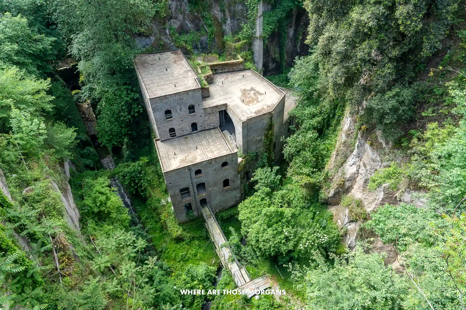 Photo of an old disused wheat mill at the bottom of a gorge covered in vegetation