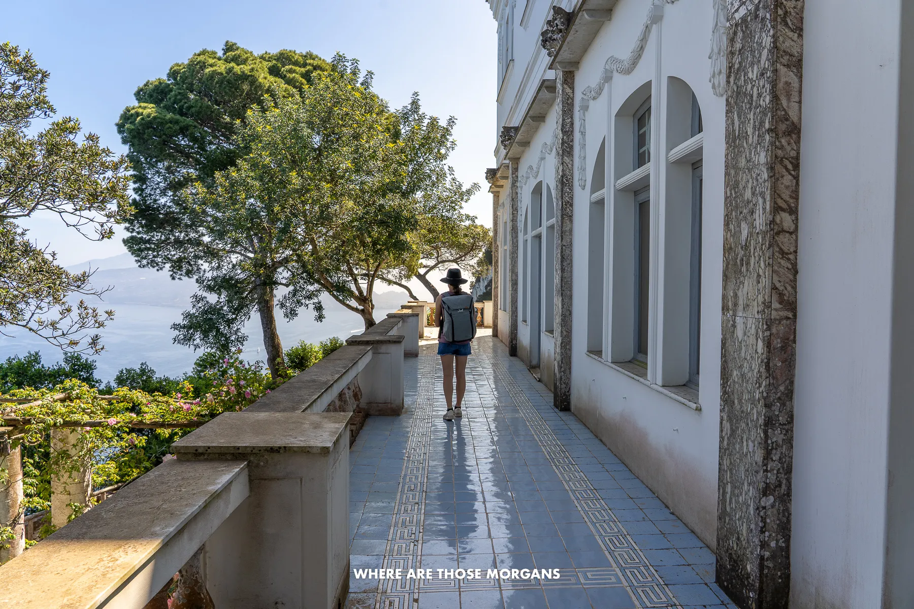 Photo of a tourist walking on a narrow balcony on the side of a villa with trees and ocean view