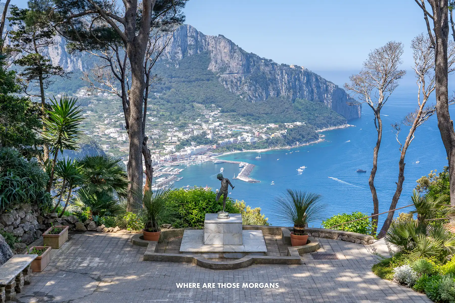 Photo of a view over Capri through trees and behind a statue high up on the east side of the island