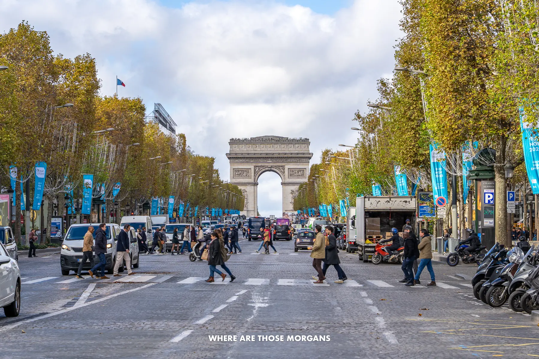 Photo of people and cars on the Champs-Elysees with trees lining the way to the Arc de Triomphe behind