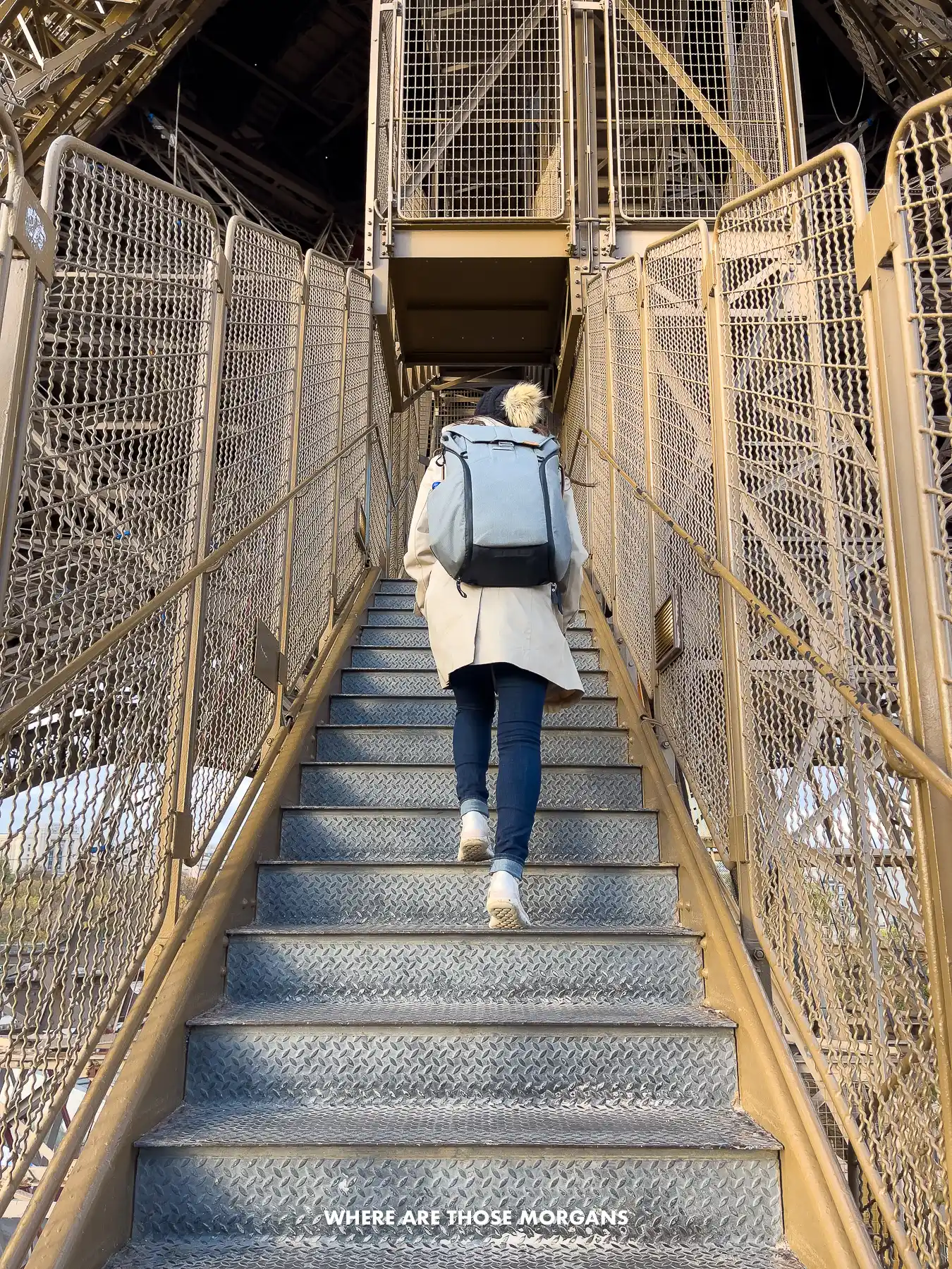 Photo of Kristen Morgan climbing up the steps of the Eiffel Tower with a coat and backpack on