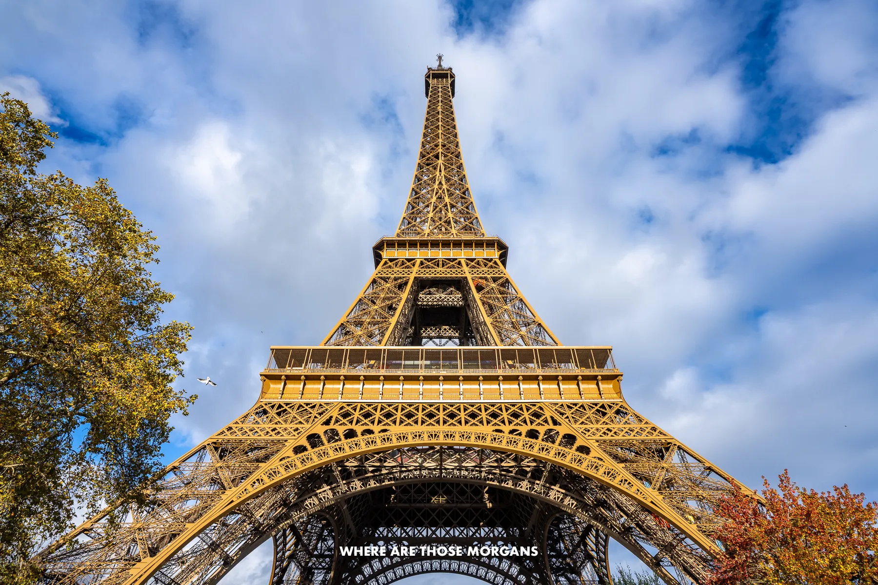 Photo of the Eiffel Tower from below looking up on a sunny day with clouds in the sky