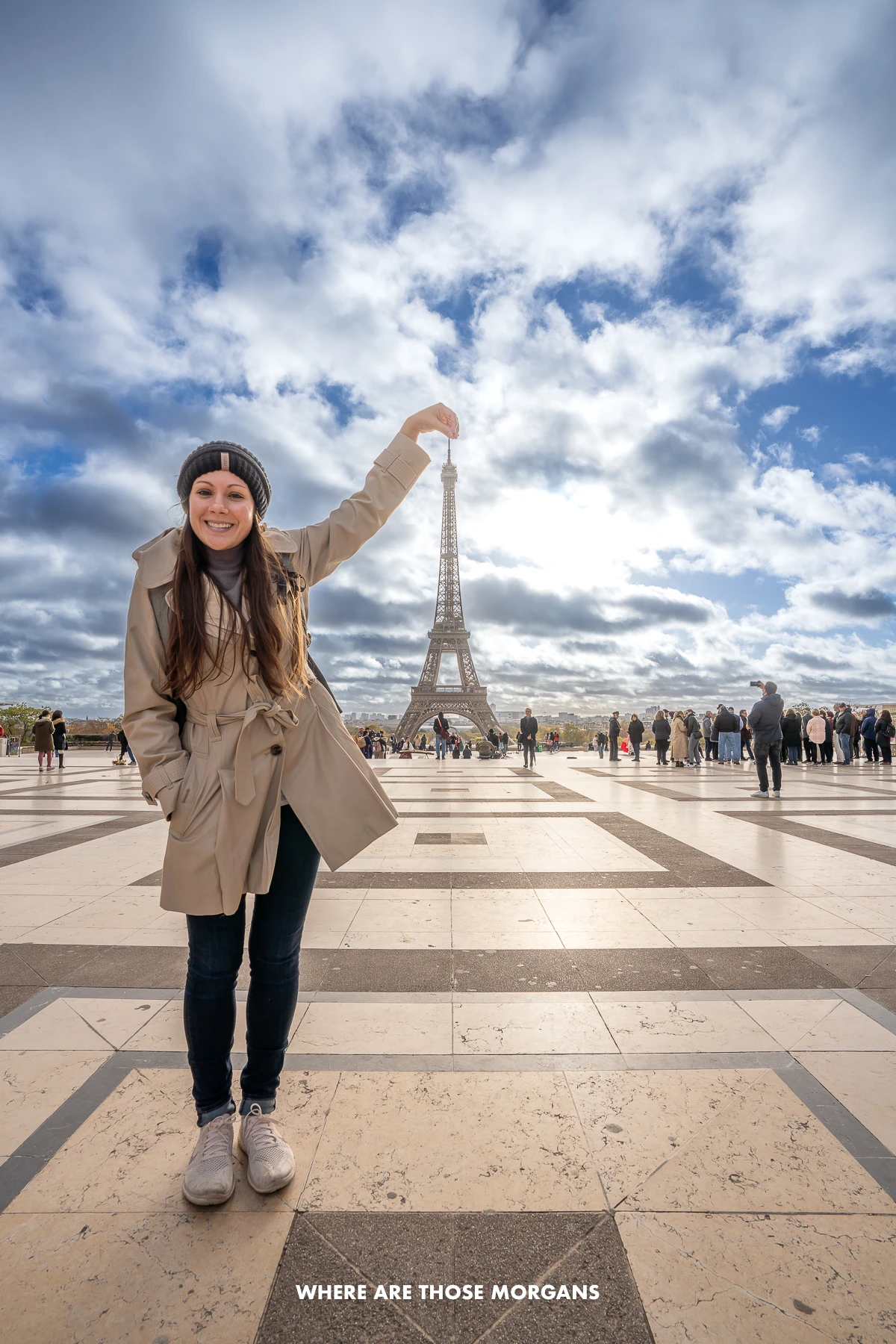 Photo of Kristen Morgan pinching the top of the Eiffel Tower from Trocadero's marble floor with patterns and the sun in the sky above