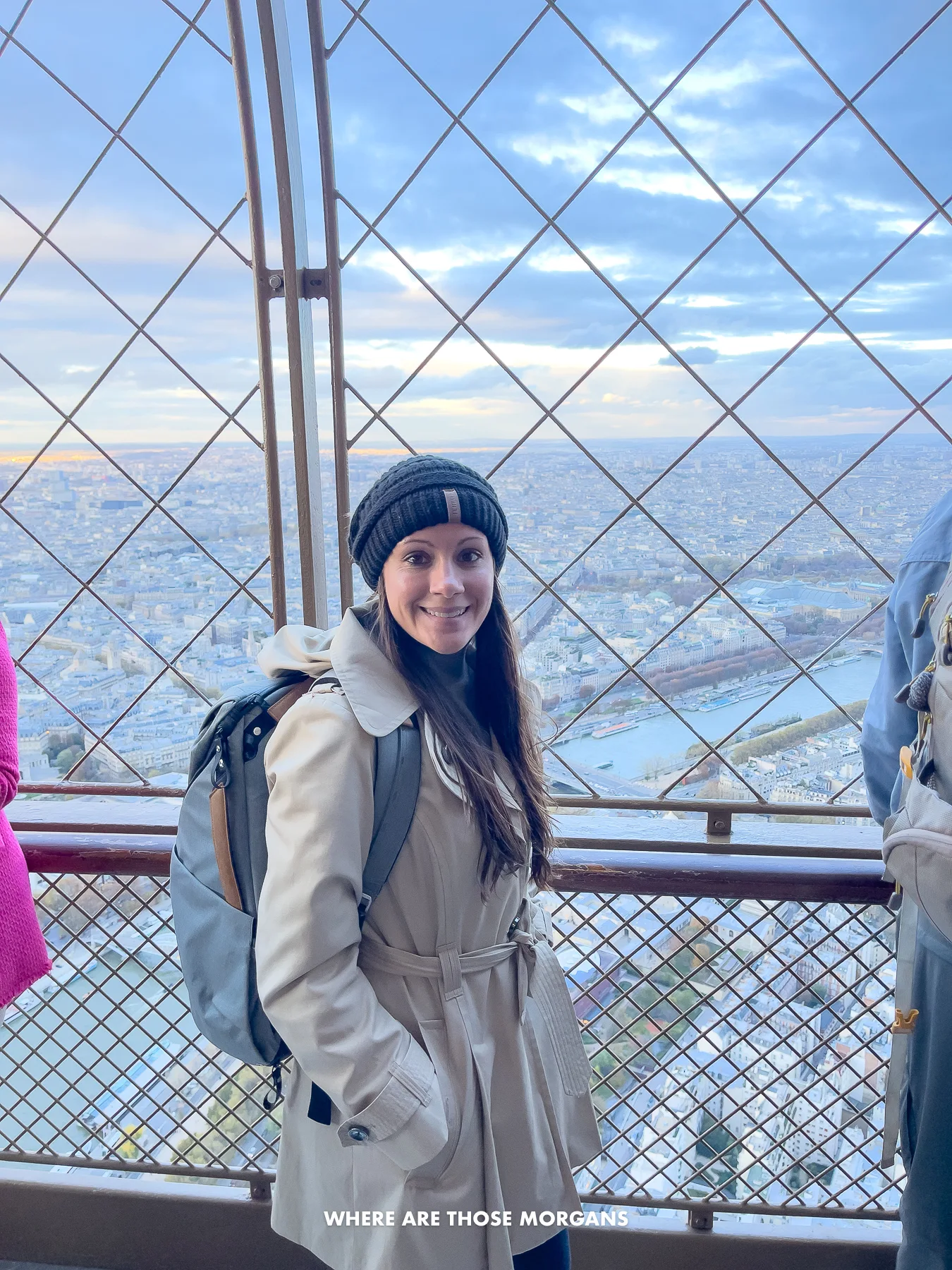 Photo of Kristen Morgan in a coat and hat at the top of the Eiffel Tower with metal mesh for safety and views over Paris