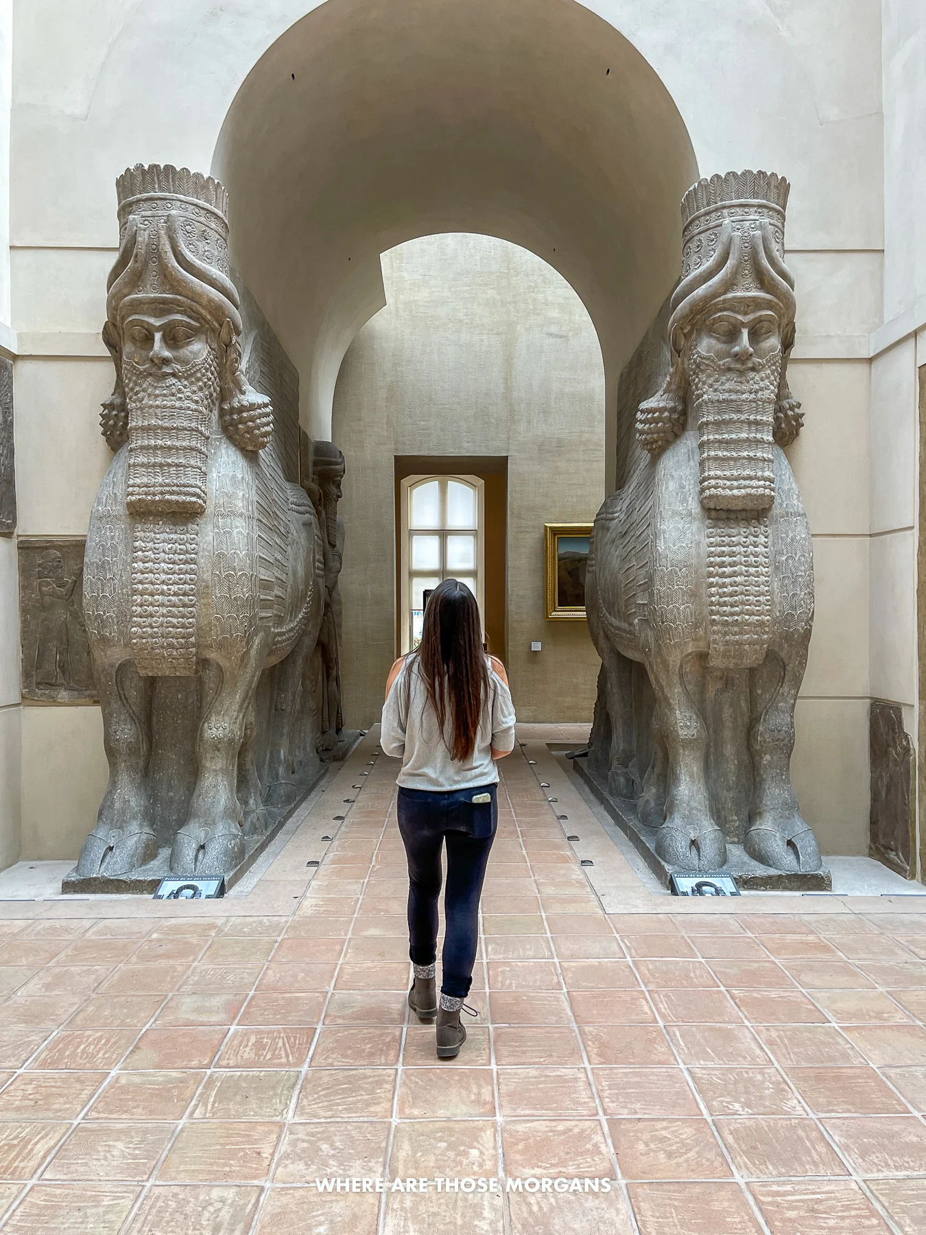 Photo of Kristen Morgan walking through an arch in a museum flanked by two large Egyptian statues
