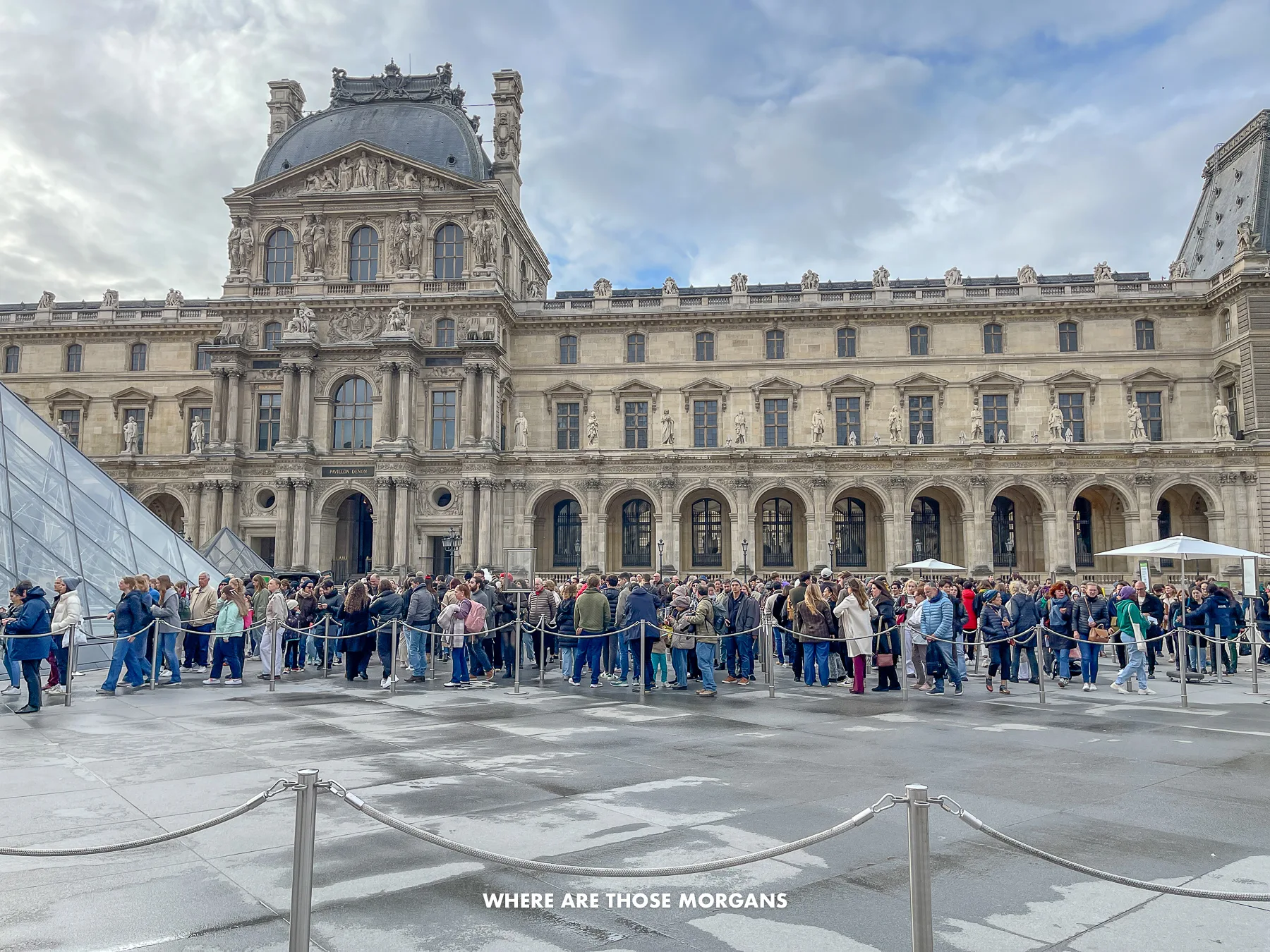 Photo of a long line of tourists standing in a courtyard waiting to get inside an attraction with a large stately building behind
