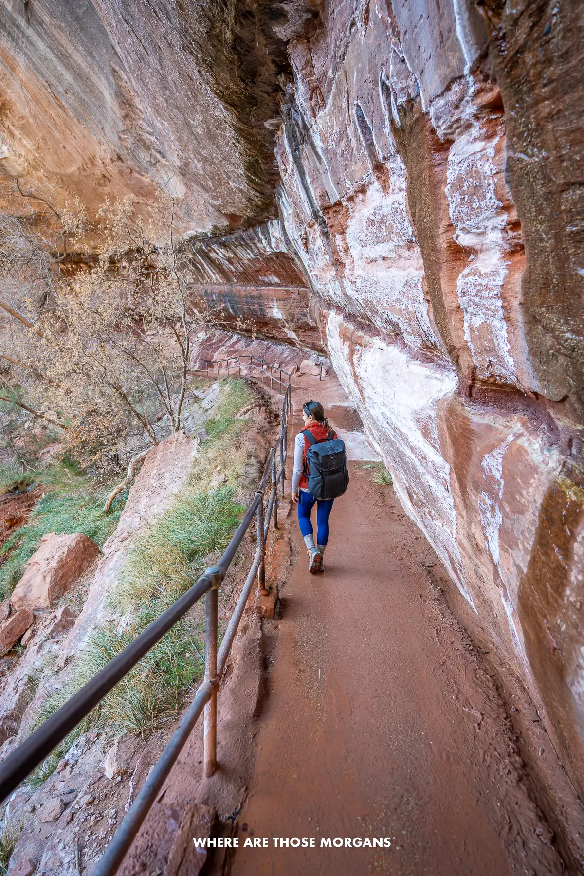 Photo of Kristen Morgan hiking on a narrow path underneath an overhanging sandstone rock formation