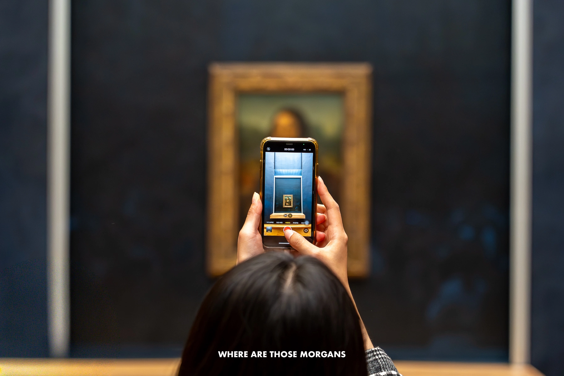 Artsy photo of hands holding up a phone which is taking a photo of the Mona Lisa in the Louvre