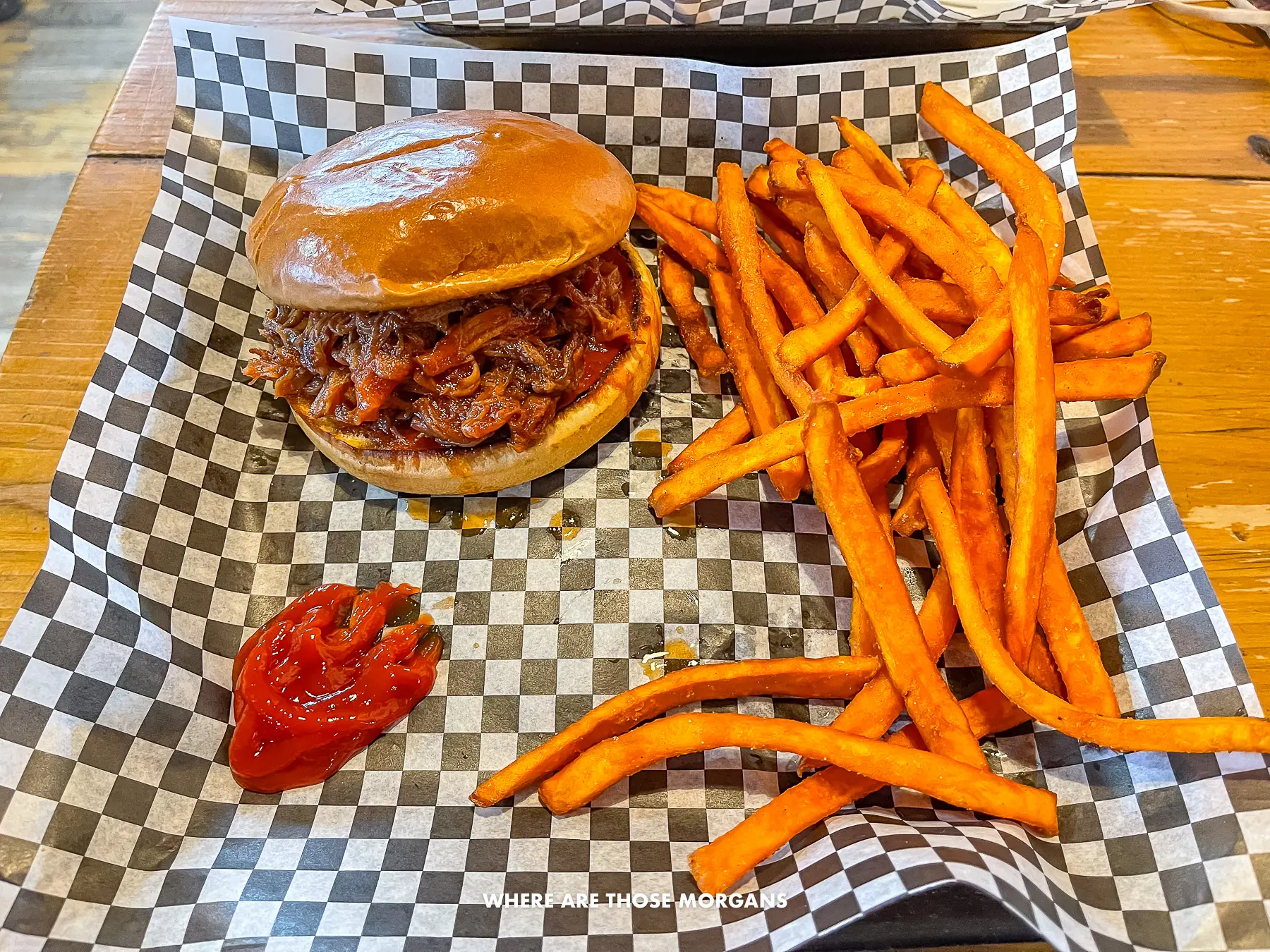 Photo of sweet potato fries and pulled pork burger on a black and white parchment paper