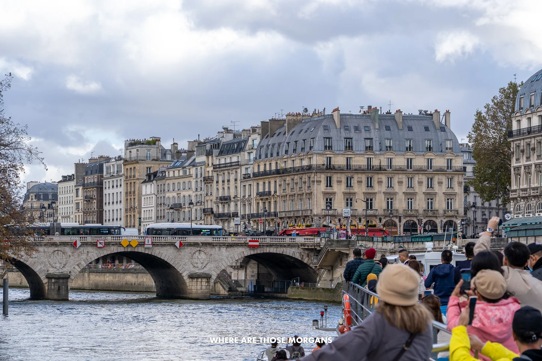 Photo of a bridge and buildings taken from a boat on a river with tourists looking at the views