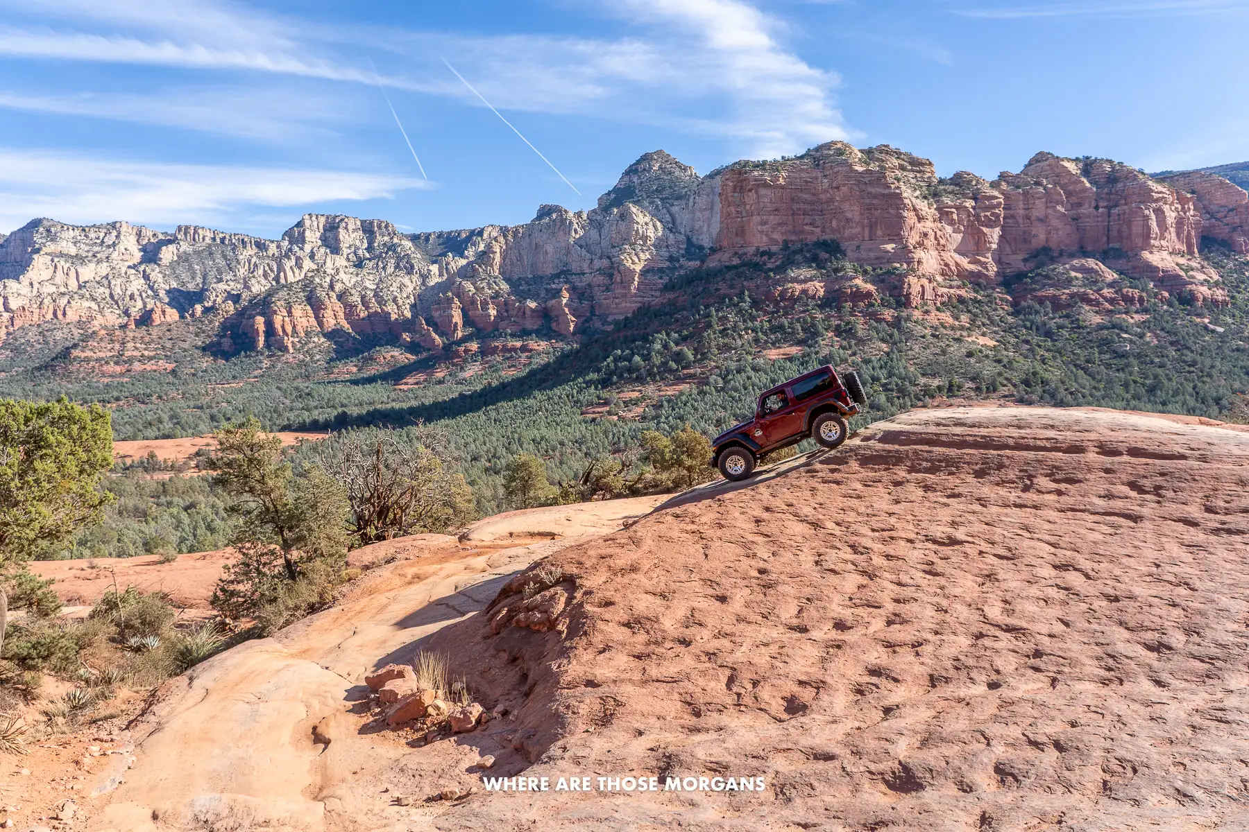 Photo of a maroon jeep slowly driving down a steep red rock formation in the Arizona desert