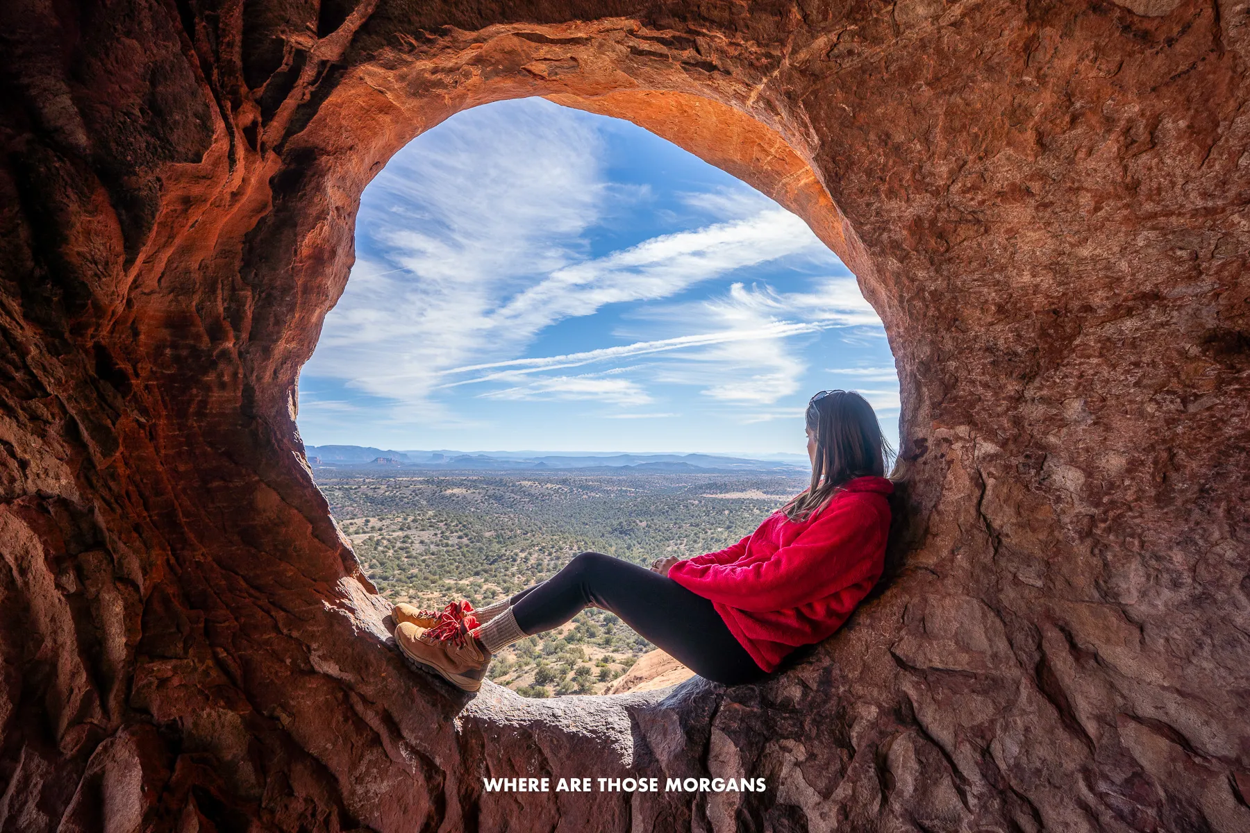 Photo of Kristen from Where Are Those Morgans sat in a round natural window of a cave in the Arizona desert