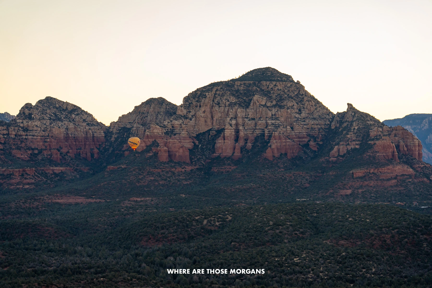 Photo of a hot air balloon rising at dawn from a valley with red and white rock cliffs behind