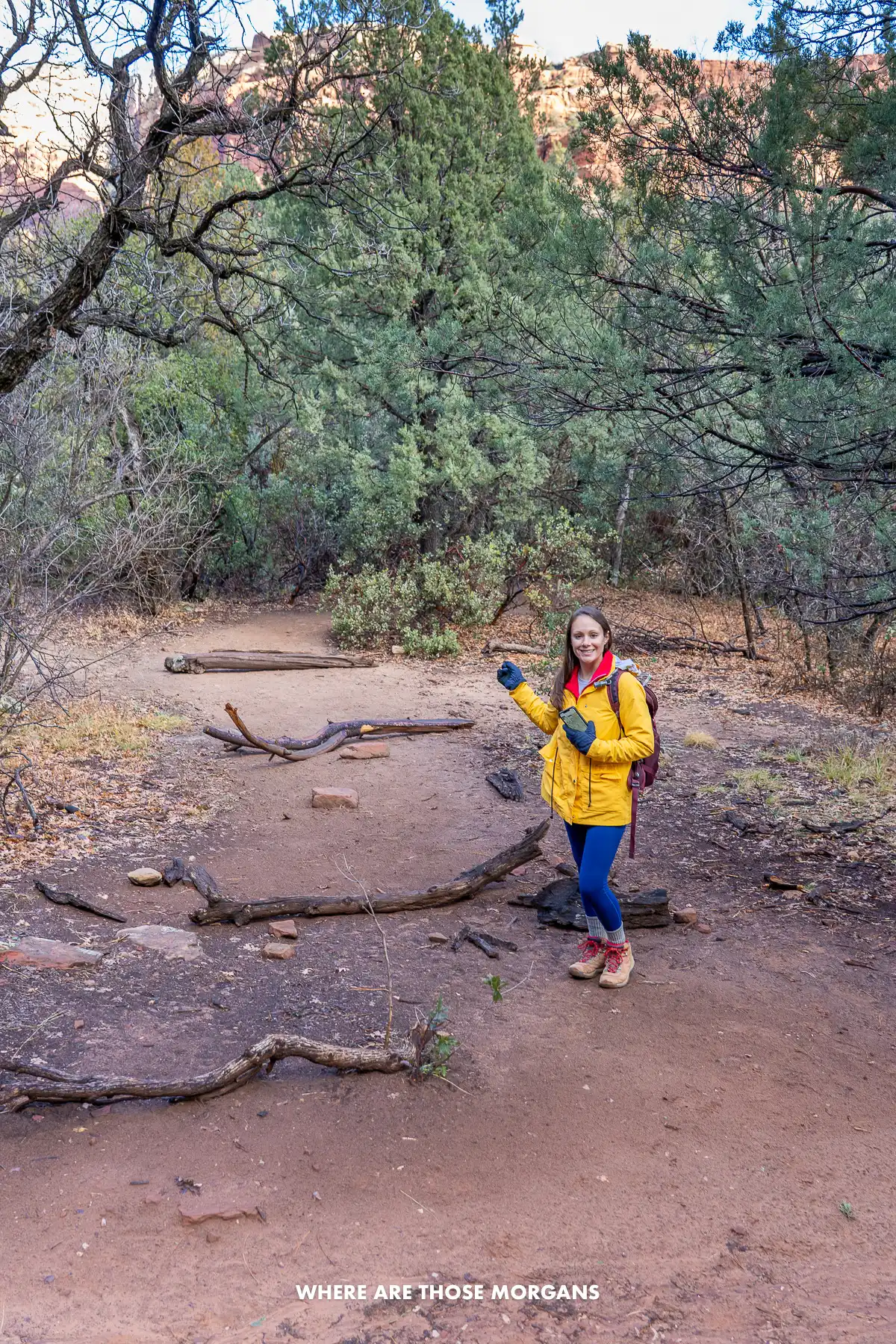 Photo of Kristen Morgan in a yellow coat pointing to a spur trail with branches on the ground