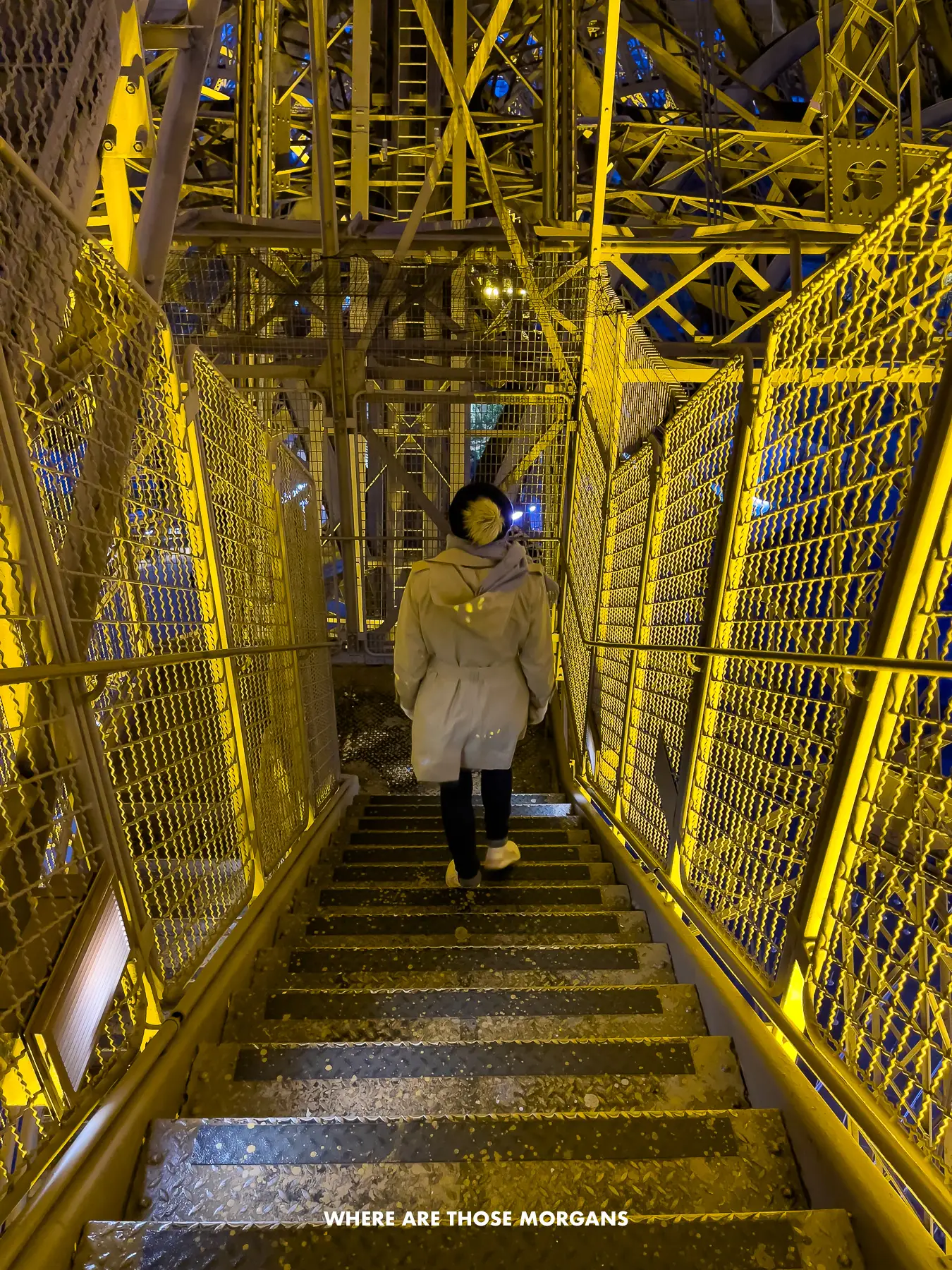Kristen from Where Are Those Morgans walking down the Eiffel Tower steps at night with the iron lattice structure glowing a yellow color