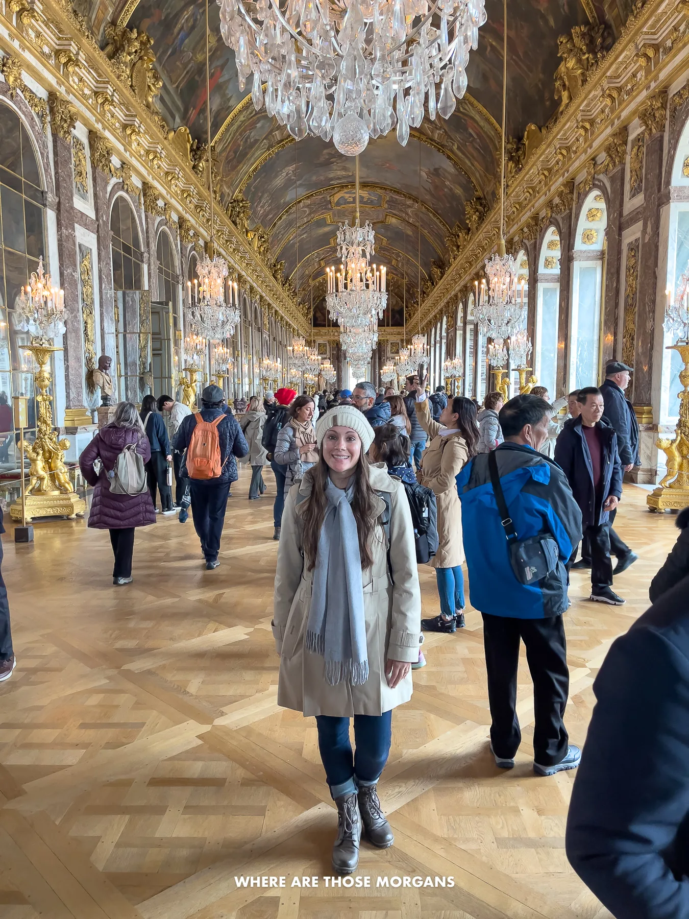 Kristen from Where Are Those Morgans standing in the middle of the Hall of Mirrors in Palace of Versailles with other tourists walking all around the room