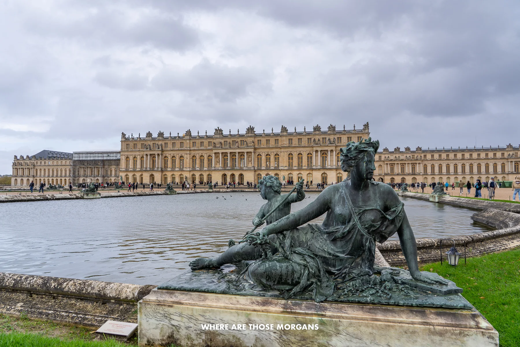 Statue on the corner of a water feature in the gardens of the Palace of Versailles with heavy clouds above