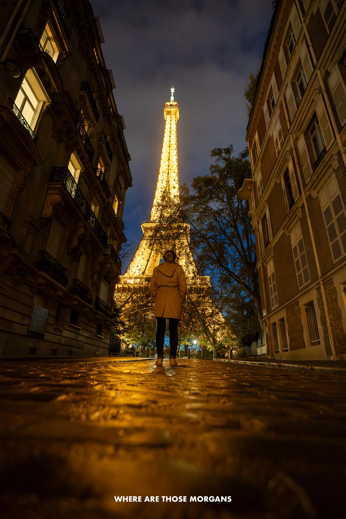 Kristen from Where Are Those Morgans walking up Avenue de l'Universite at night with the Eiffel Tower lit up behind