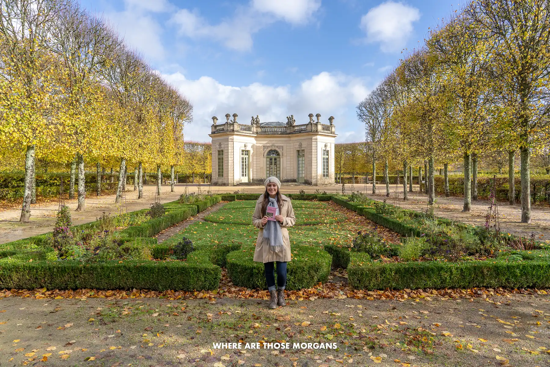 Kristen from Where Are Those Morgans standing in a beautiful manicured garden with trees lining both sides and a small building in the background