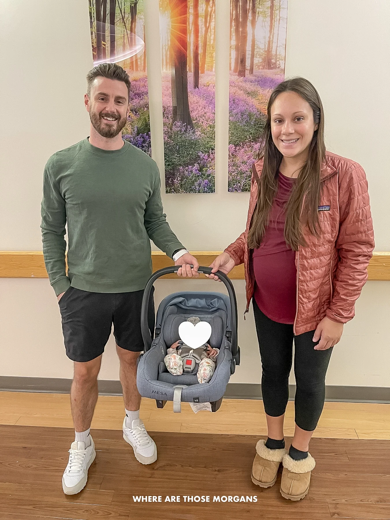 Photo of a couple in hospital maternity ward holding a baby in a car seat