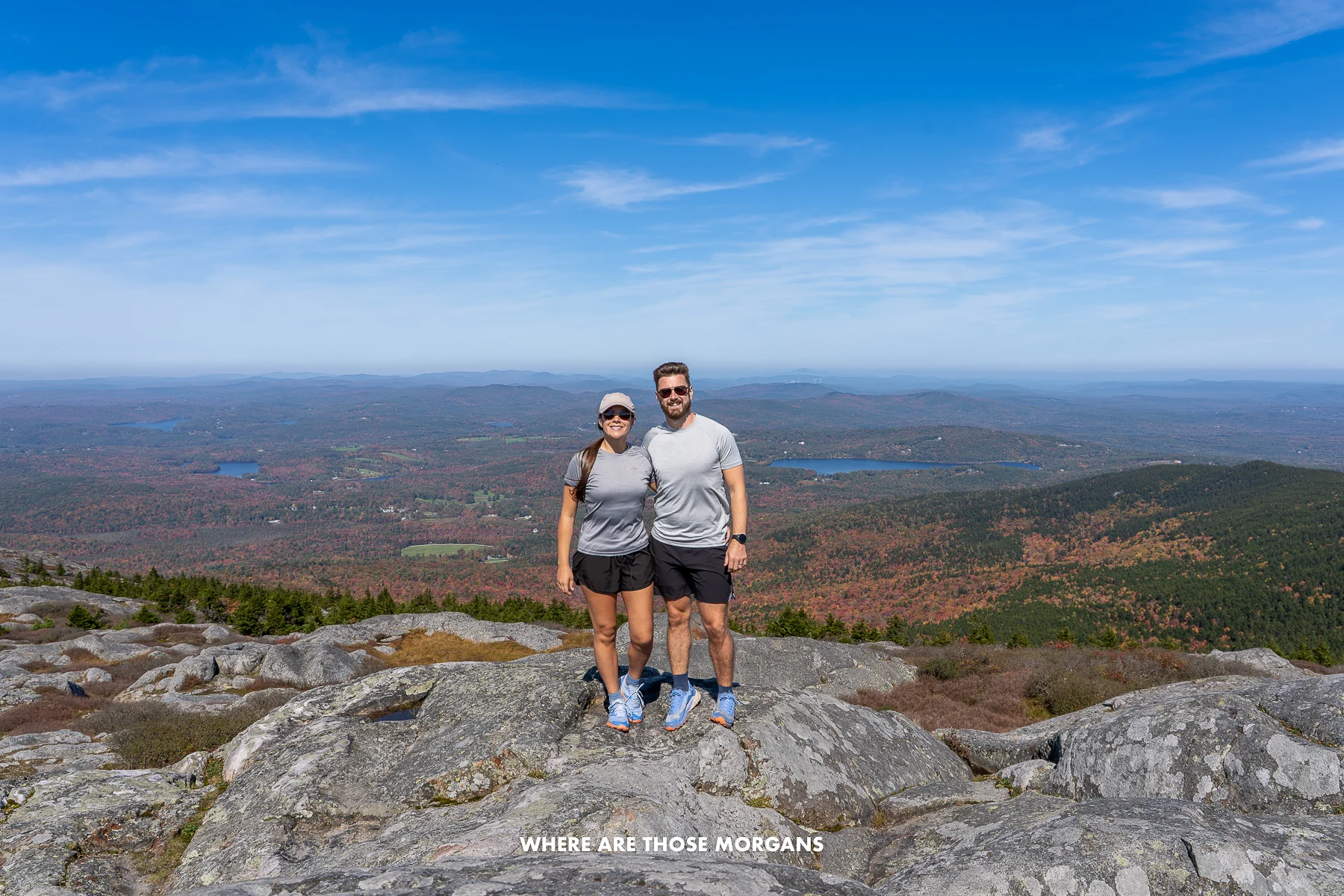 Photo of two hikers stood together on a rocky summit with far reaching wide open views over a rural landscape in New England in the fall