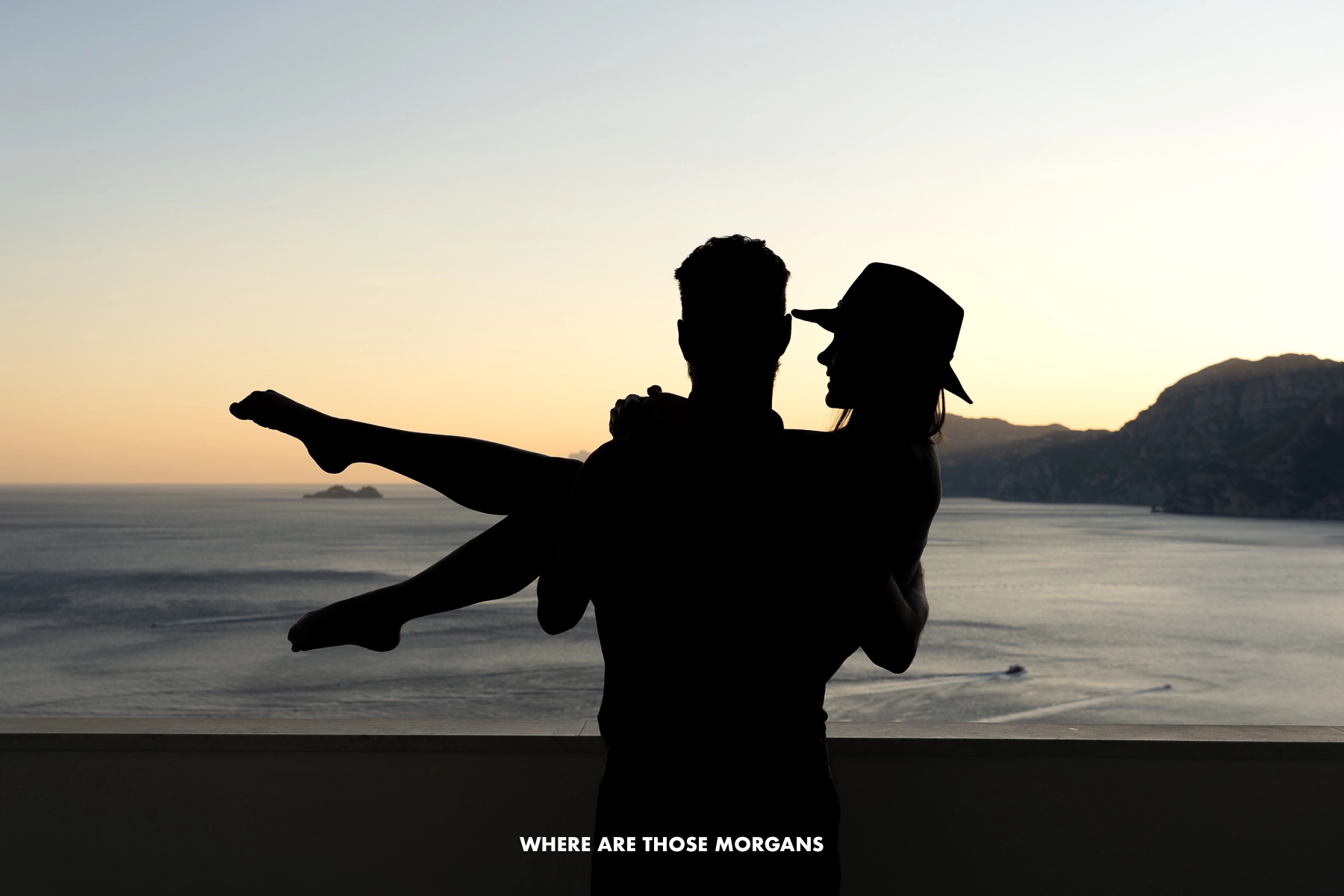 Photo of silhouetted tourists on a hotel balcony overlooking the ocean at sunset in Italy