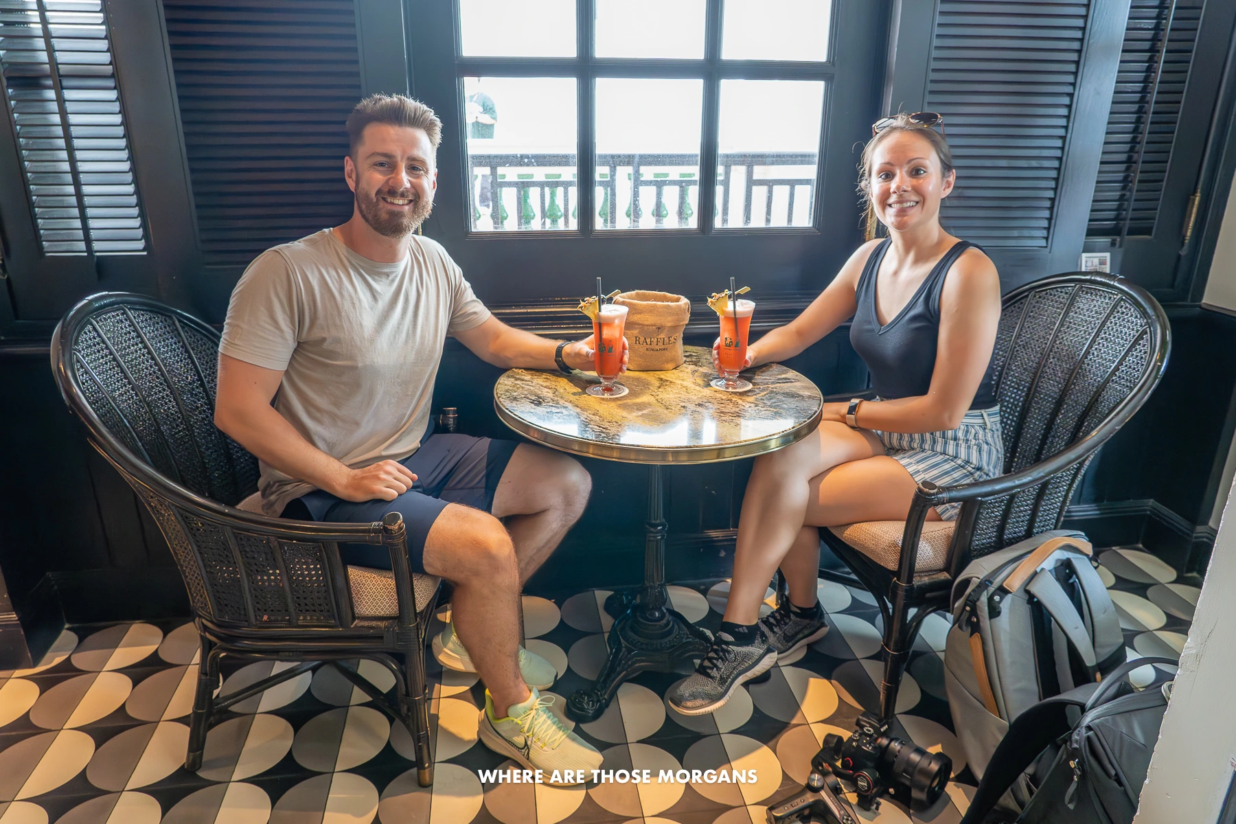 Photo of a couple sat at a small table with cocktails inside Raffles in Singapore
