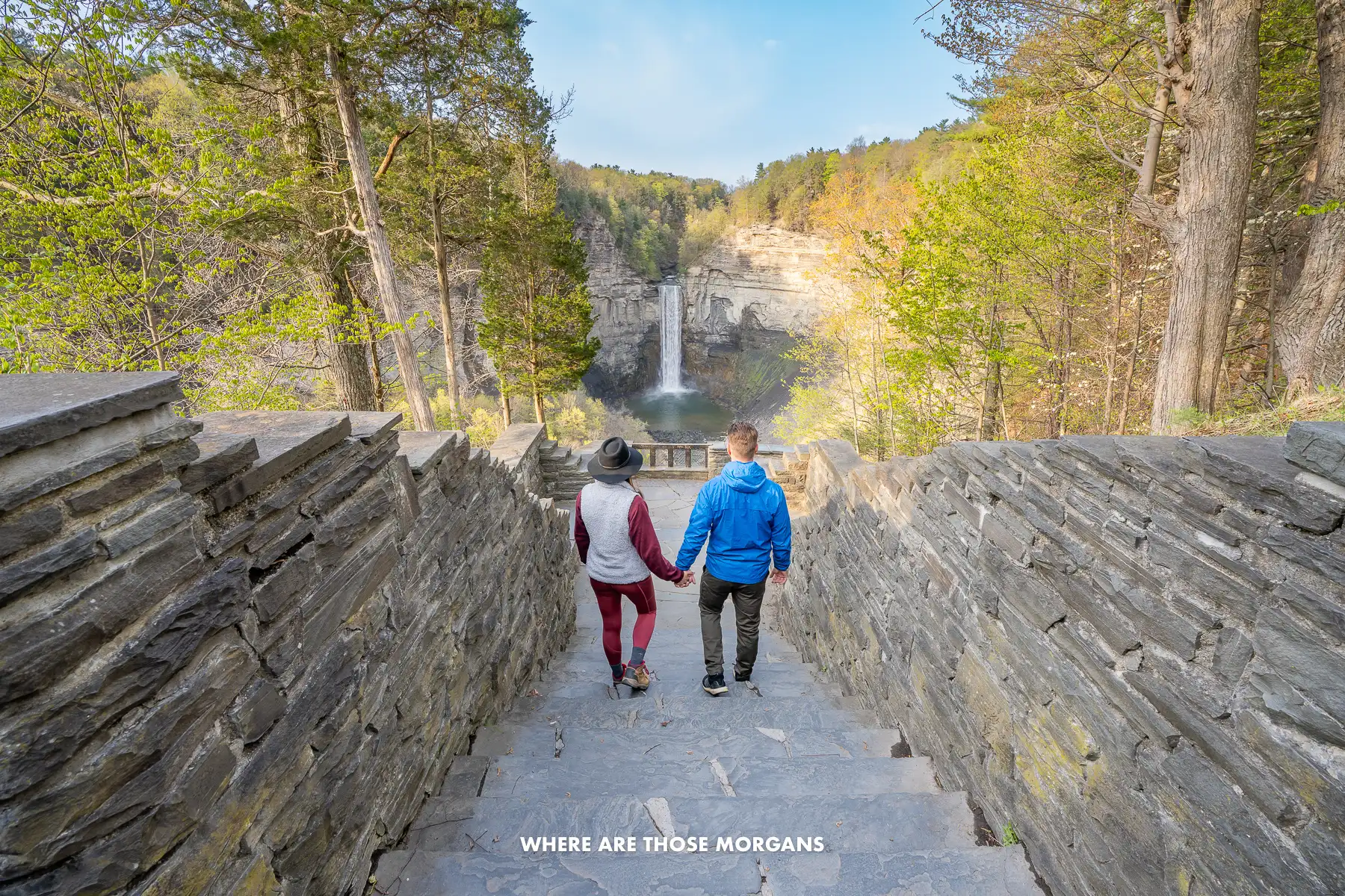 Photo of a couple walking down stone steps together holding hands with views over a waterfall and fall foliage colors