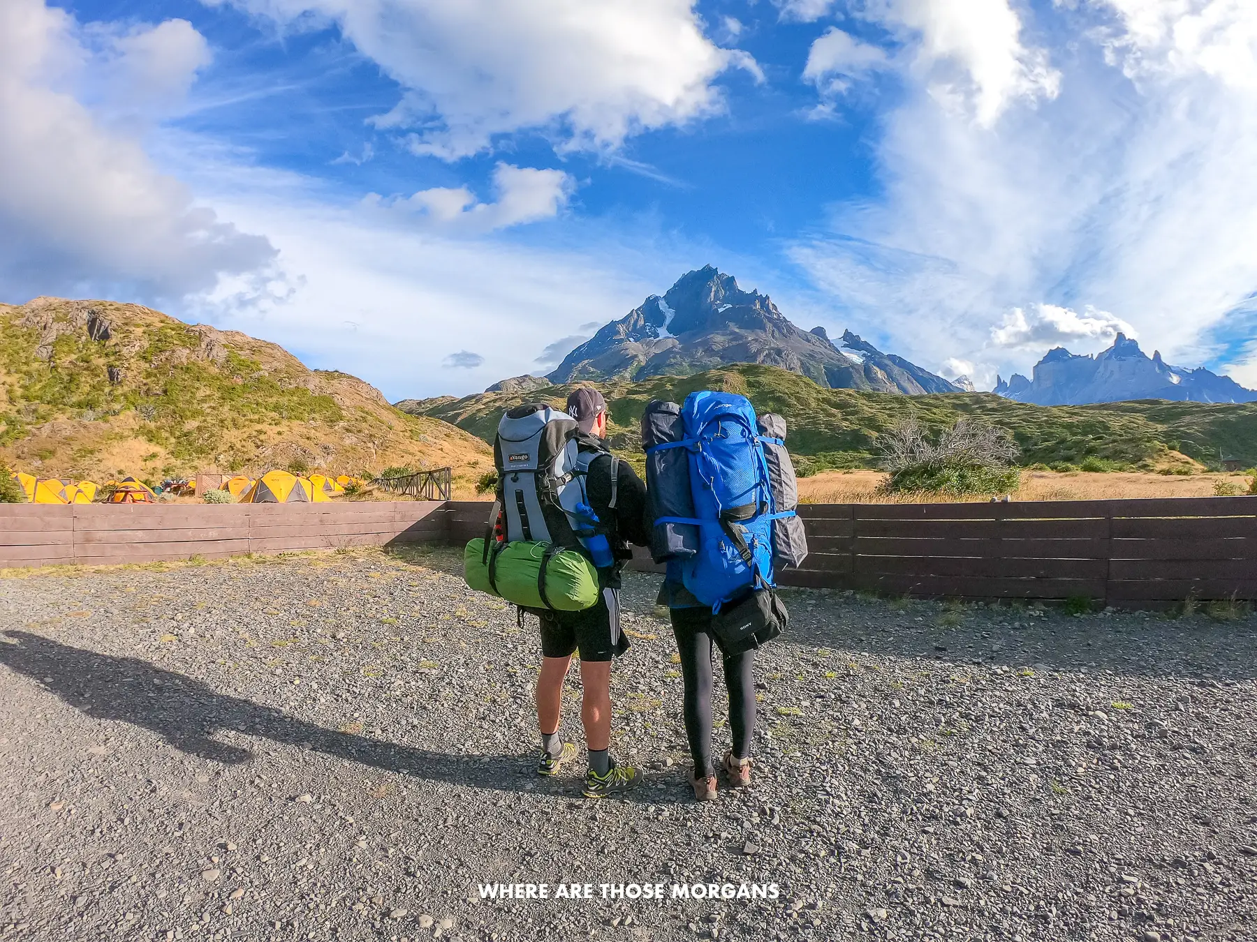 Photo of the back side of two hikers with huge backpacks in a mountainous landscape on a sunny day