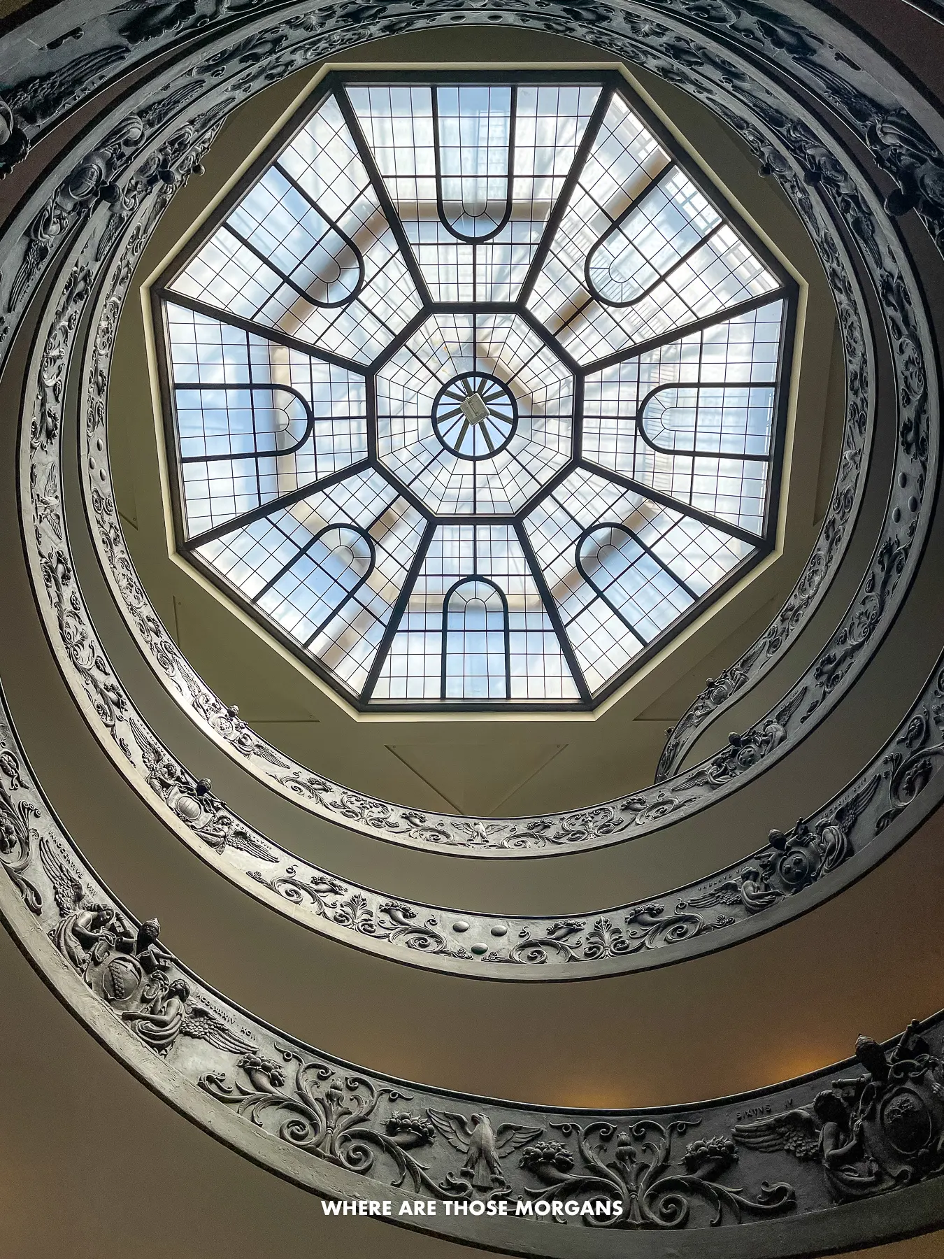 Looking up through a double helix staircase through a glass roof at the top