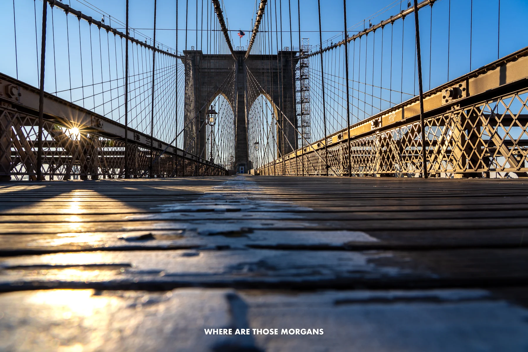 Brooklyn Bridge wooden pedestrian walkway completely empty at sunrise with the sun bursting through metal rails