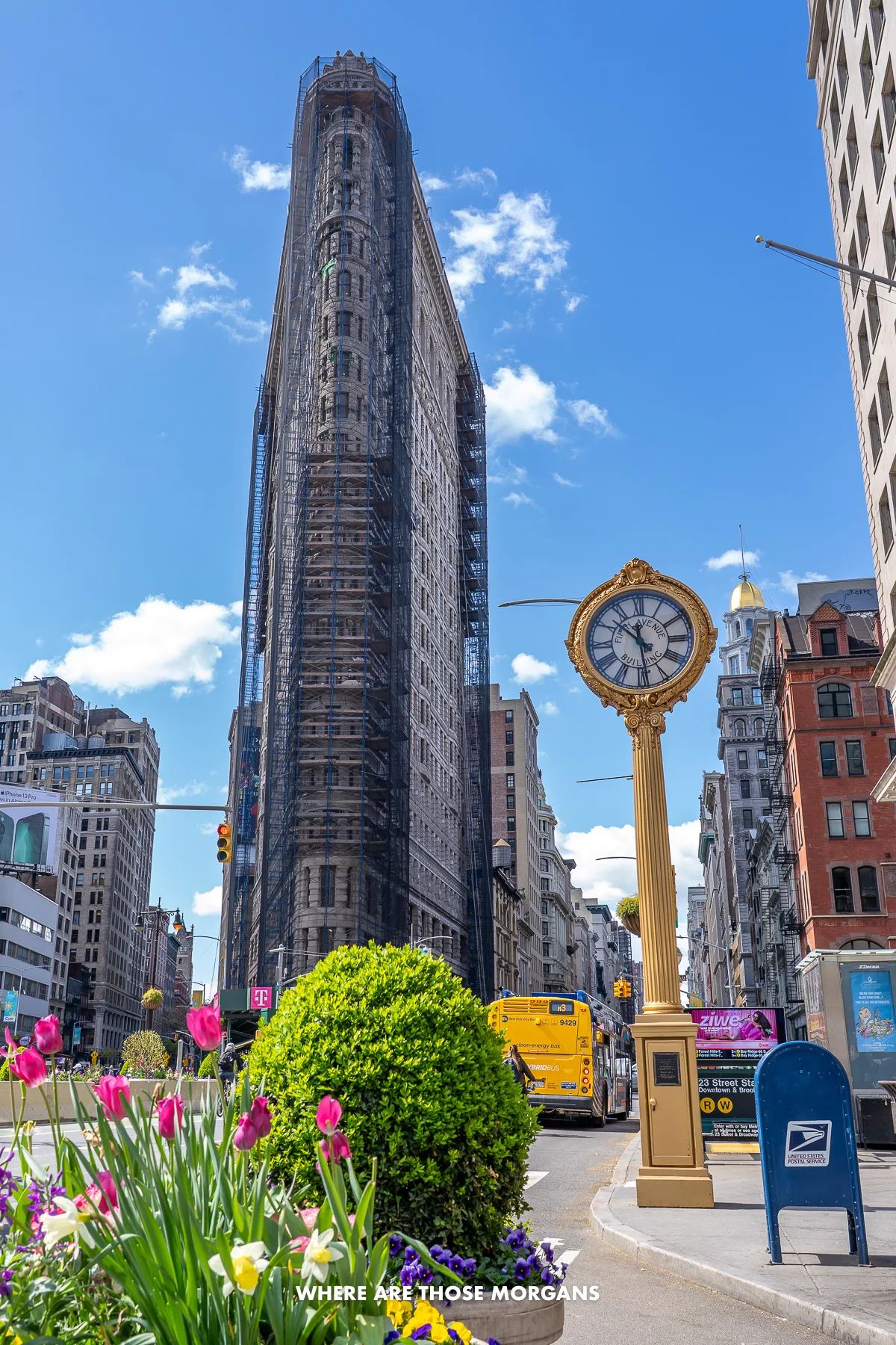 The Flatiron Building in New York with scaffolding next to the golden clock on a clear sunny day