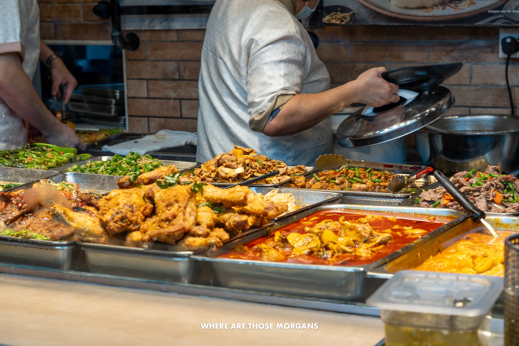Different kinds of cooked food in hot plates with a chef behind