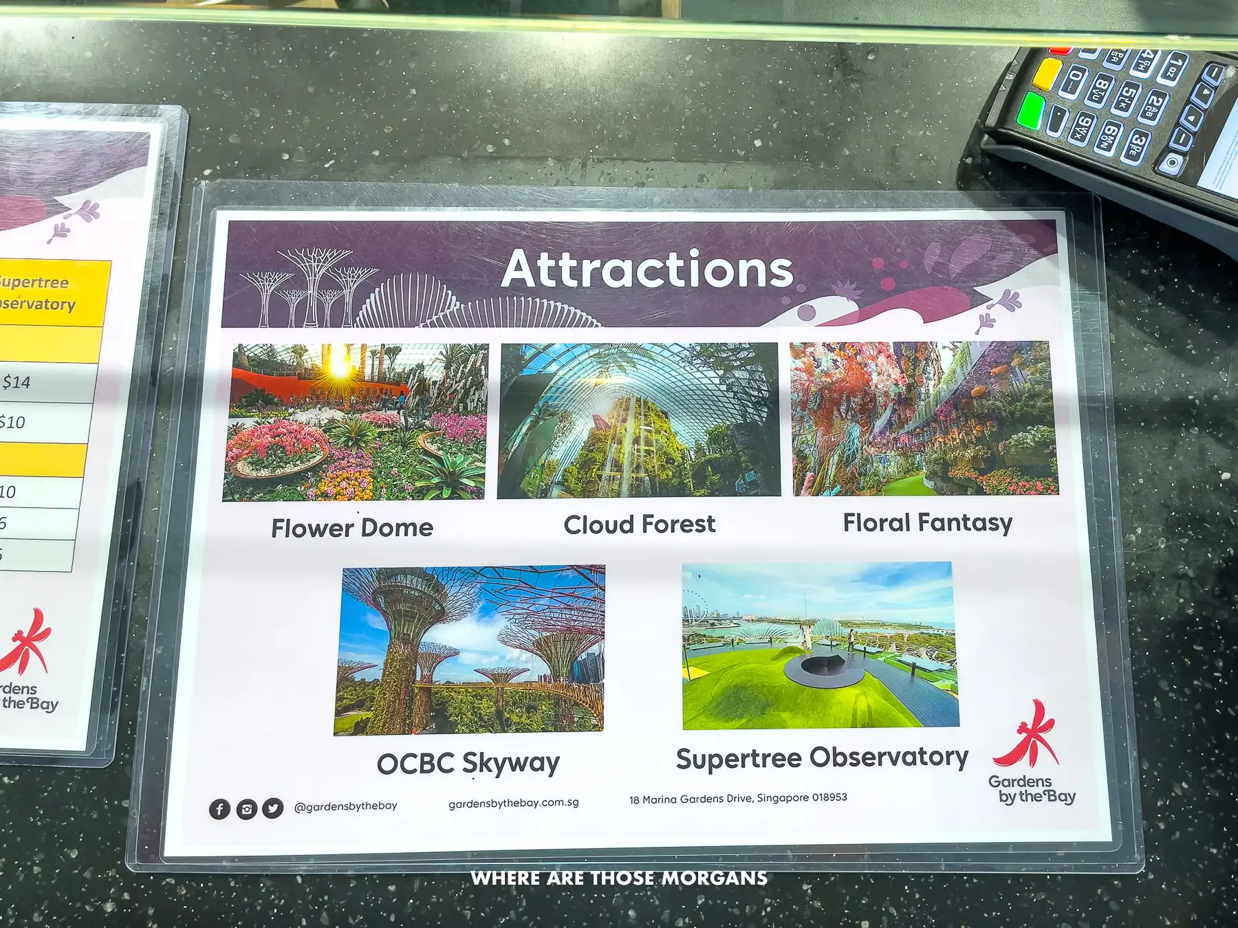 Laminated paper showing photos of the 5 attractions available at Gardens by the Bay in Singapore on a ticket desk counter next to a chip and pin payment device