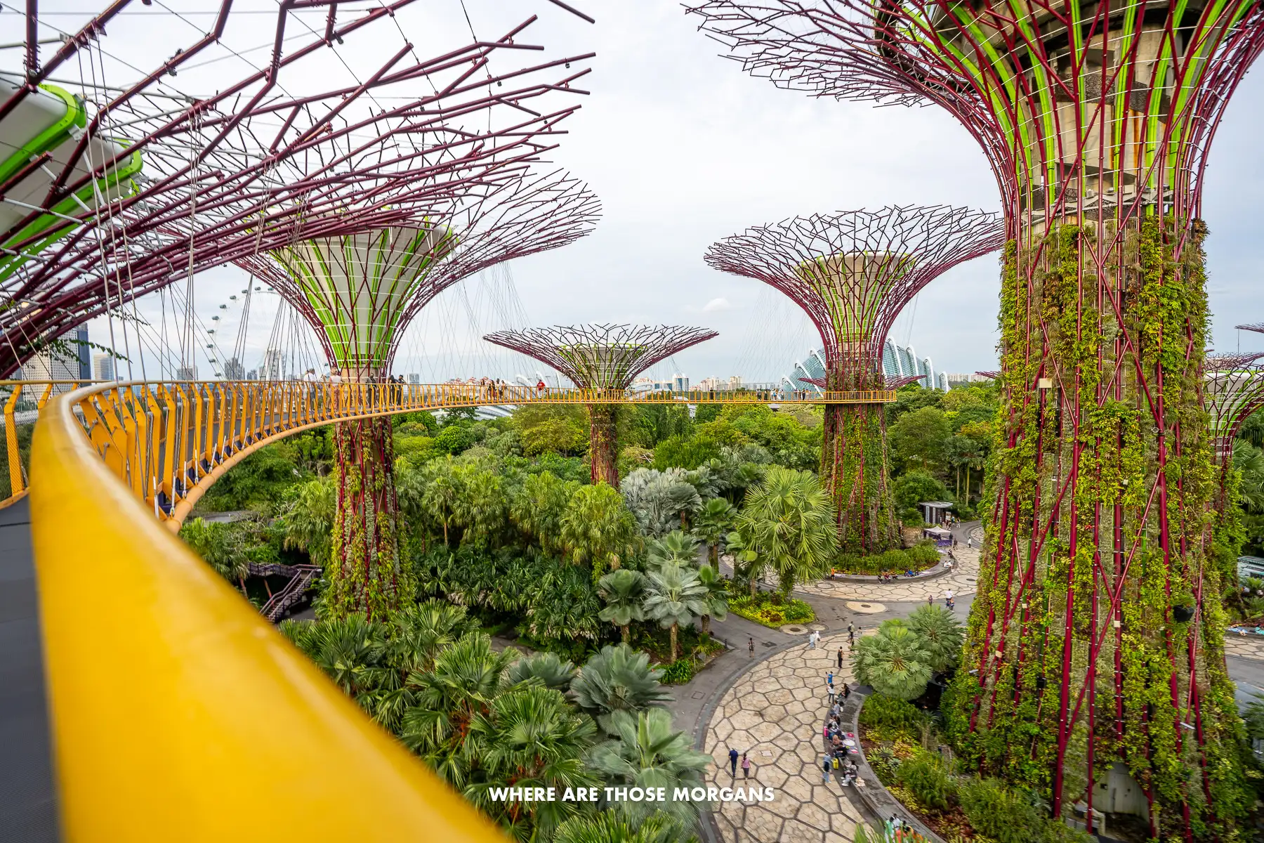 Looking along a curving yellow rail on a bridge between lots of tall fake trees