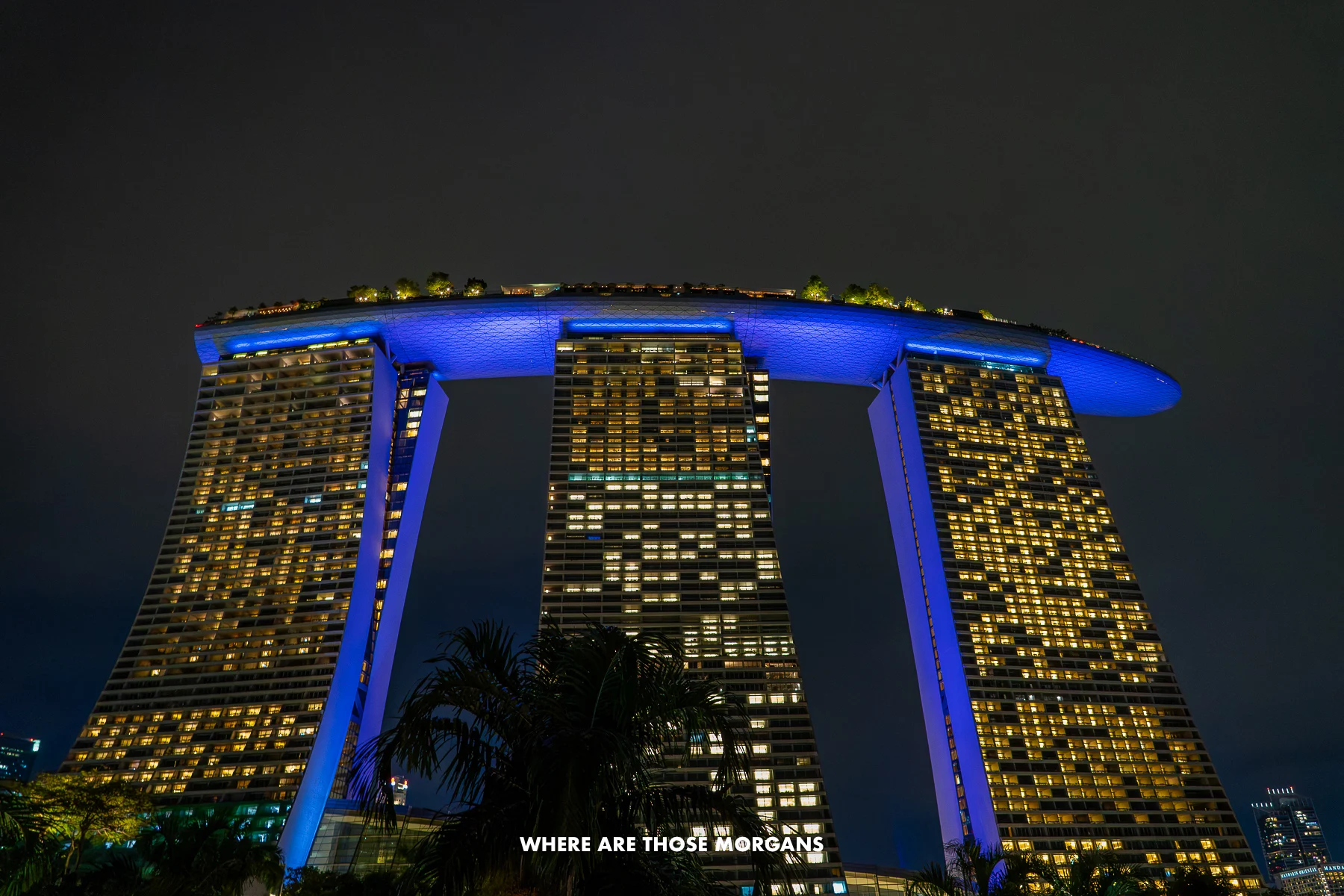 The three towers and curving roof of Marina Bay Sands hotel lit up against a pitch black sky