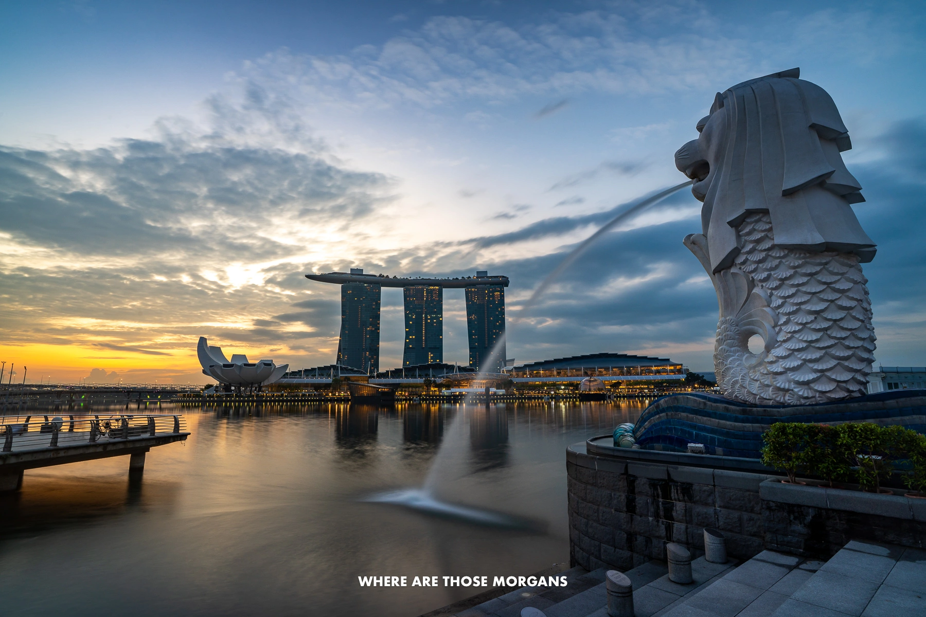 The Merlion of Singapore squirting water into Marina Bay with the famous hotel behind at sunrise