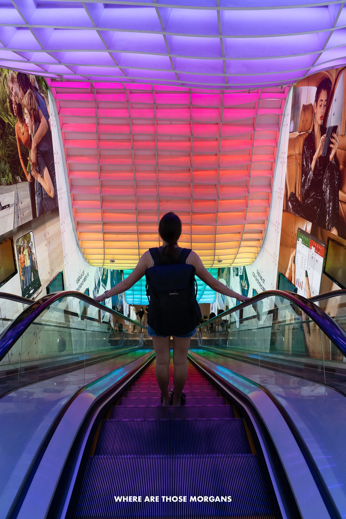 Kristen from Where Are Those Morgans going down an escalator under colorful lights into one of Orchard's futuristic looking shopping malls