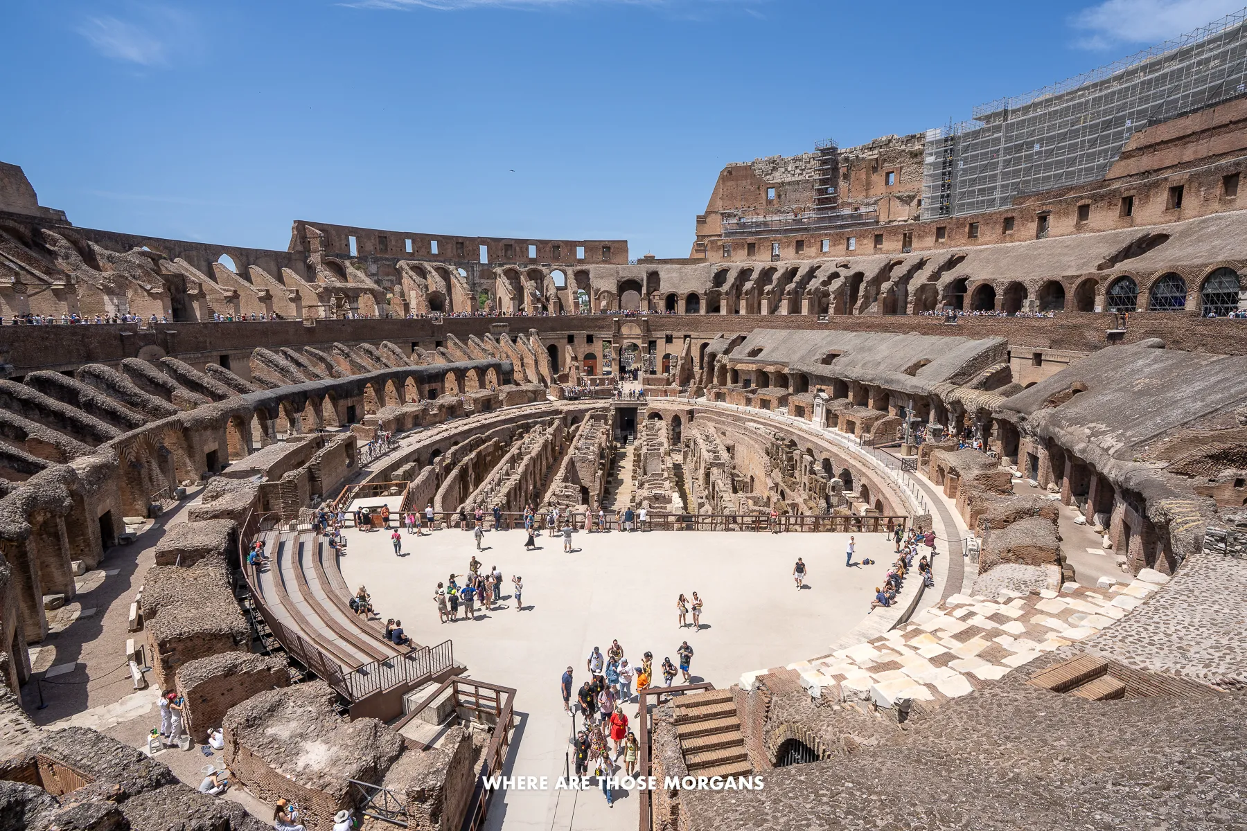 Inside the Colosseum of Rome from the second floor looking over the arena, underground and crowds on a clear day with blue skies
