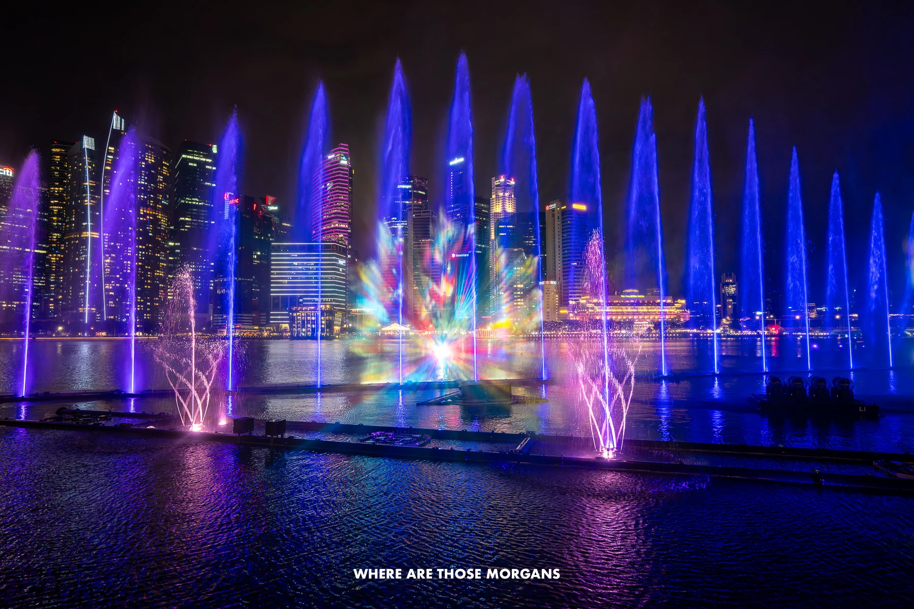 A light and water show with fountains dancing and blue lights over a bay at night