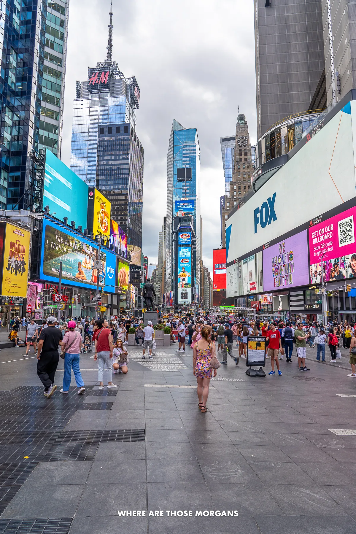 Tourists walking through the bright lights of Times Square on a cloudy day